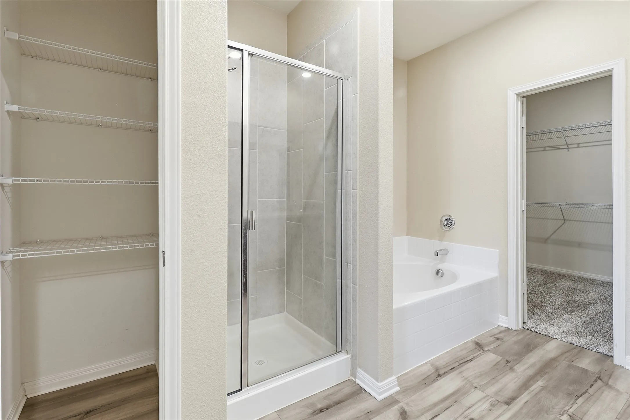 Modern bathroom featuring a glass-enclosed shower with tile surround, a soaking tub with chrome fixtures, and wood-finish flooring