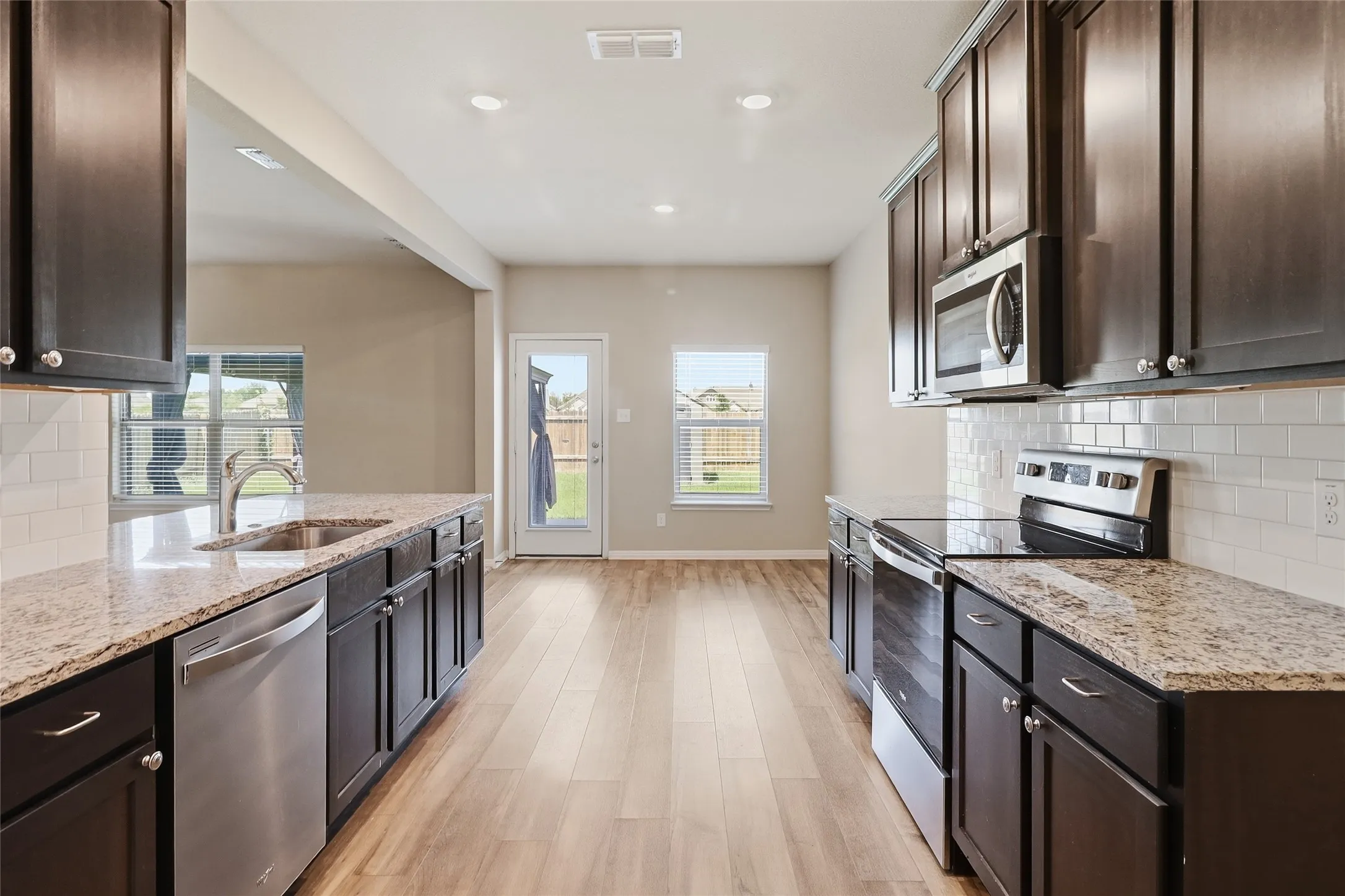 Modern kitchen featuring dark wood cabinetry, granite countertops, and stainless steel appliances including a built-in microwave, dishwasher, and range