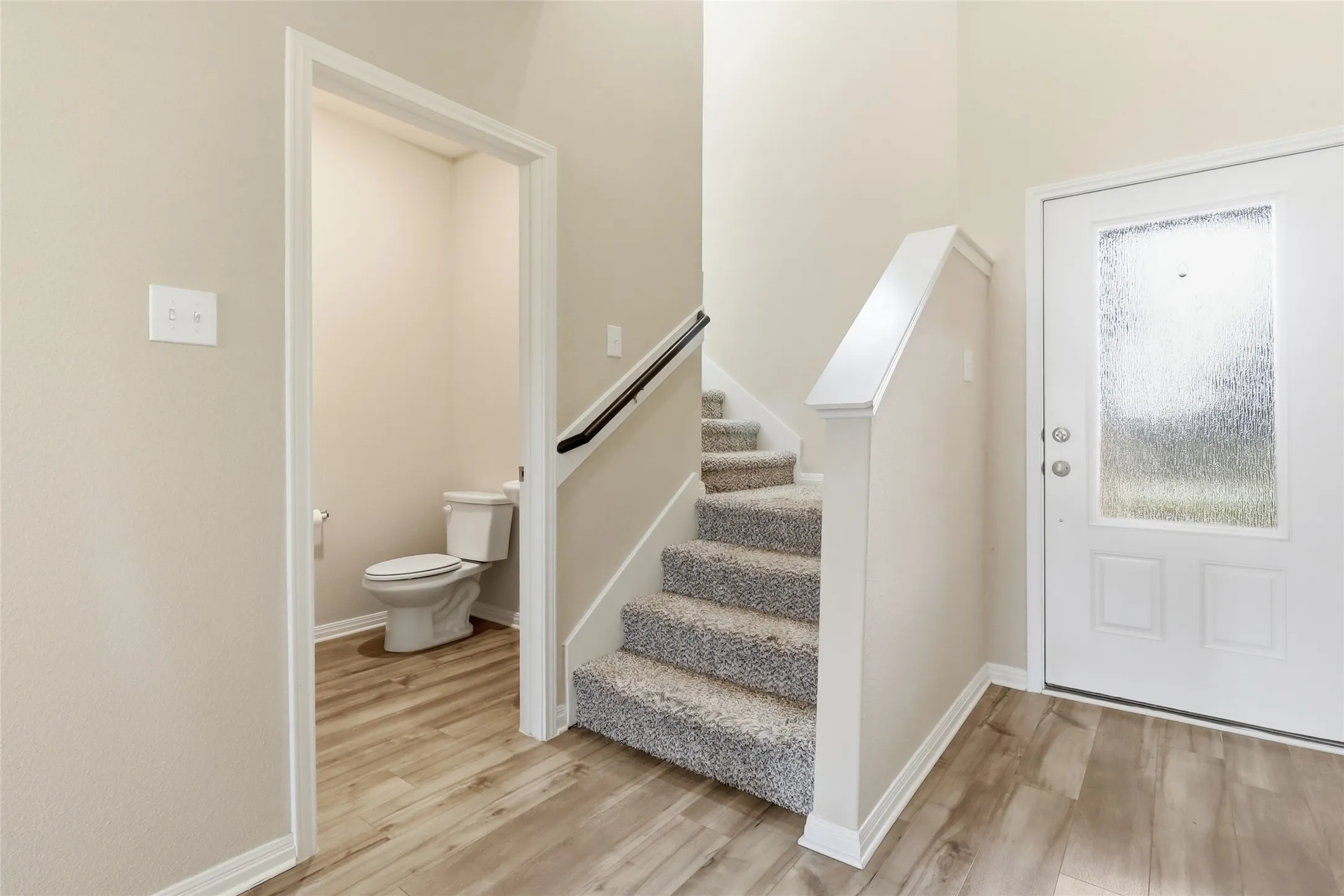 Entryway featuring wood-finish flooring, a carpeted staircase, and a white front door with obscure glass