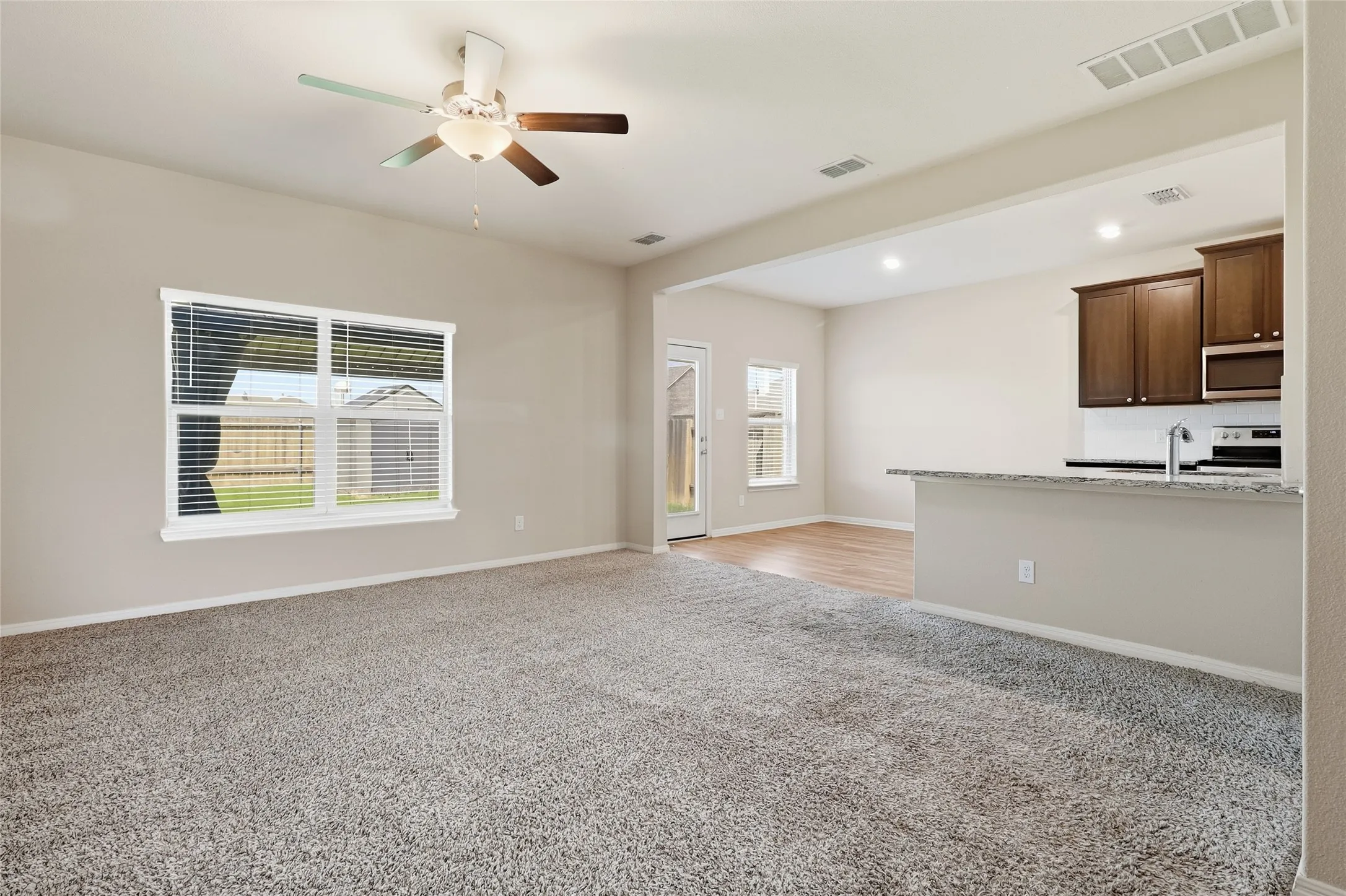 Spacious living area featuring neutral carpeting and a ceiling fan