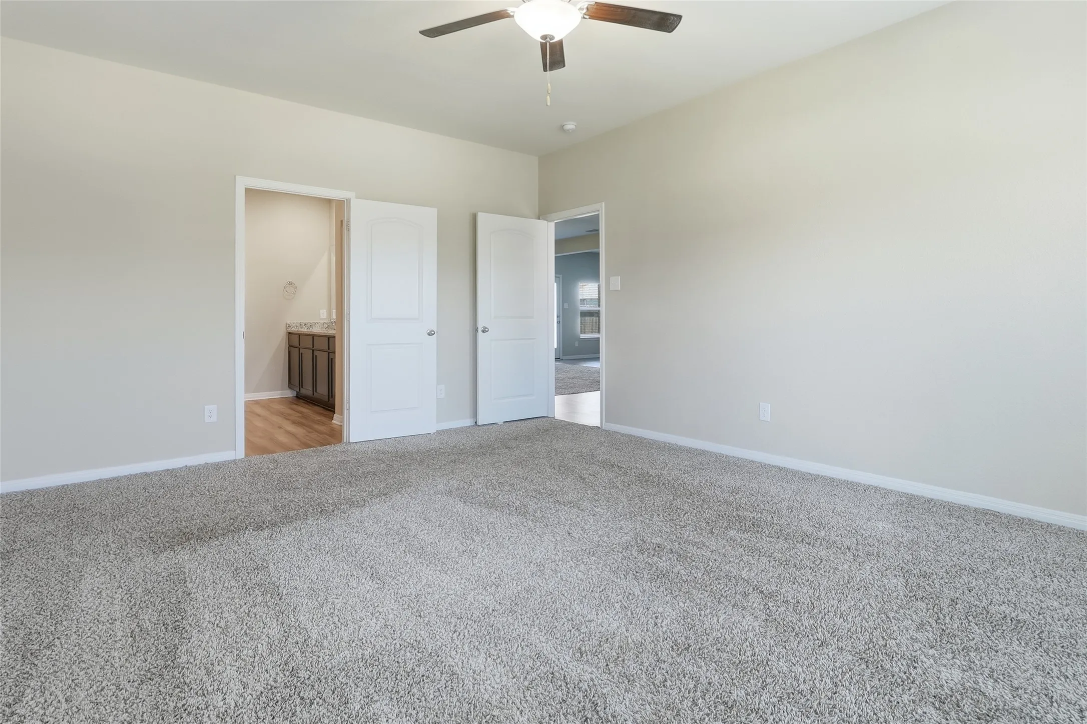 Spacious room featuring light-toned walls, plush grey carpeting, and a ceiling fan with integrated lighting