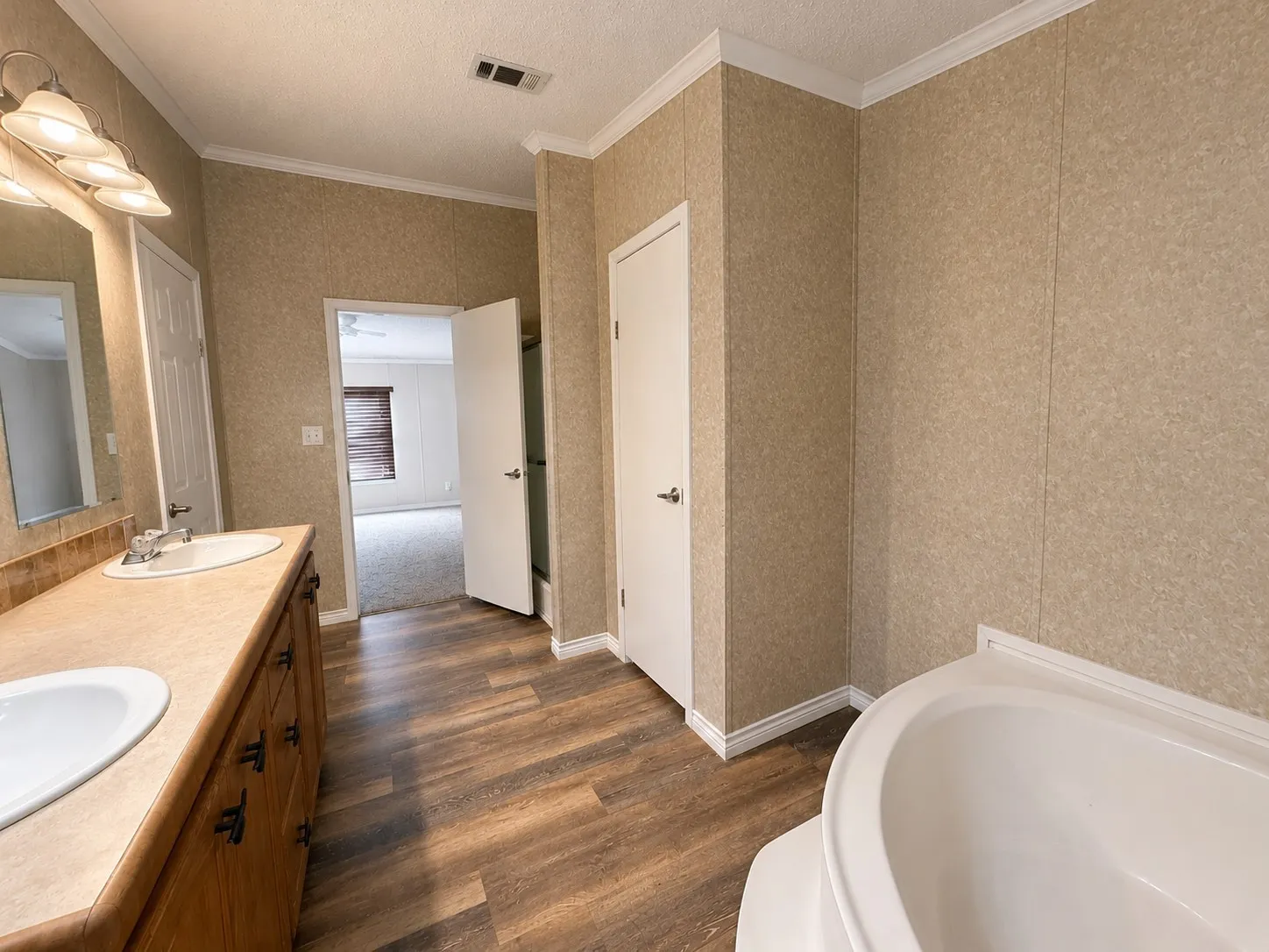 Bathroom featuring a double vanity with integrated sinks, wood-finish cabinetry, a drop-in soaking tub, wood-finish flooring, and crown molding