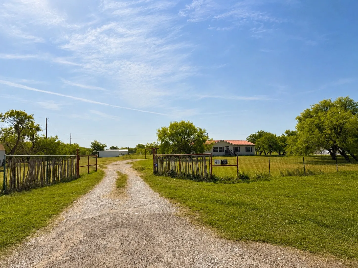 Gravel driveway providing access to the property, bordered by a rustic wooden fence and lush green grass