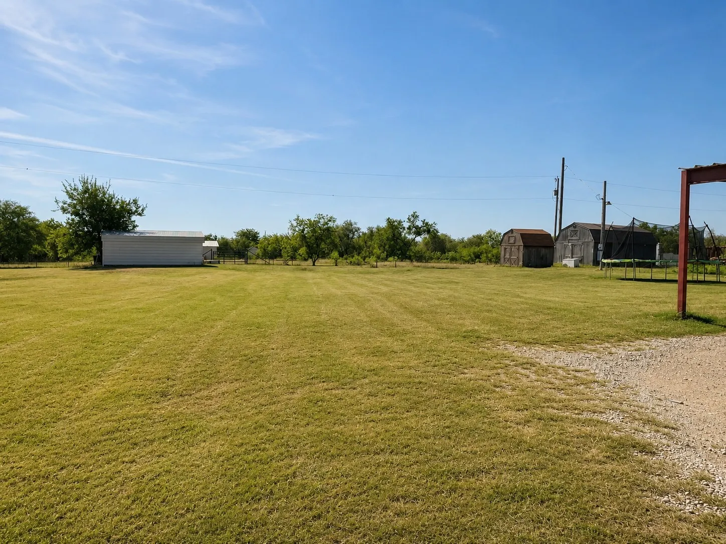 Expansive grassy area with multiple outbuildings including a white metal structure and two wooden sheds