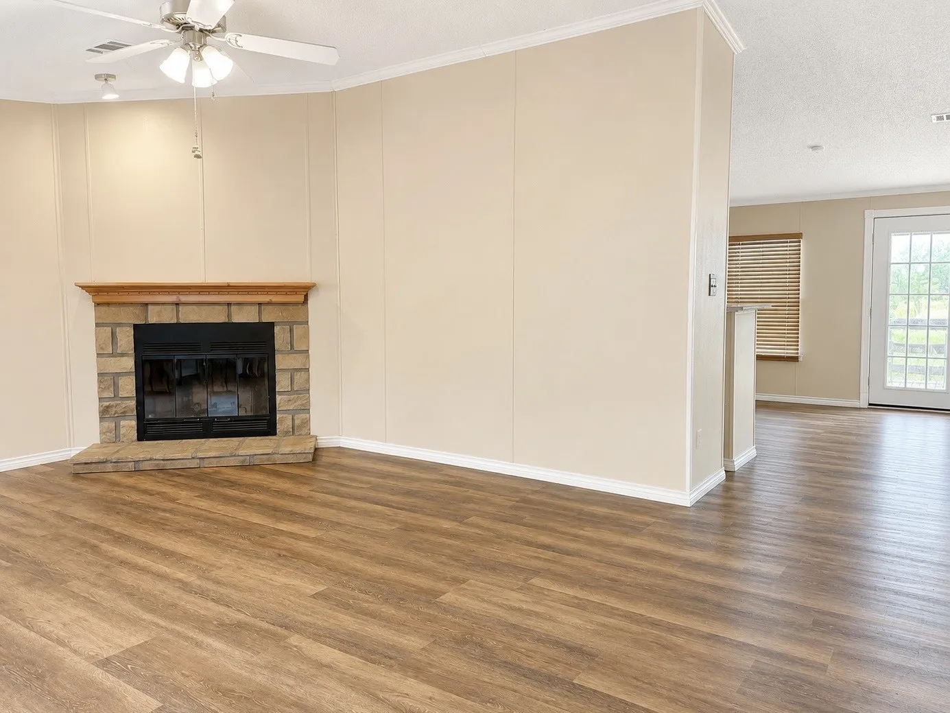 Living area featuring wood-finish flooring, a stone-surround fireplace with a wood mantle, a ceiling fan with integrated lighting, and a white paneled door with glass inserts