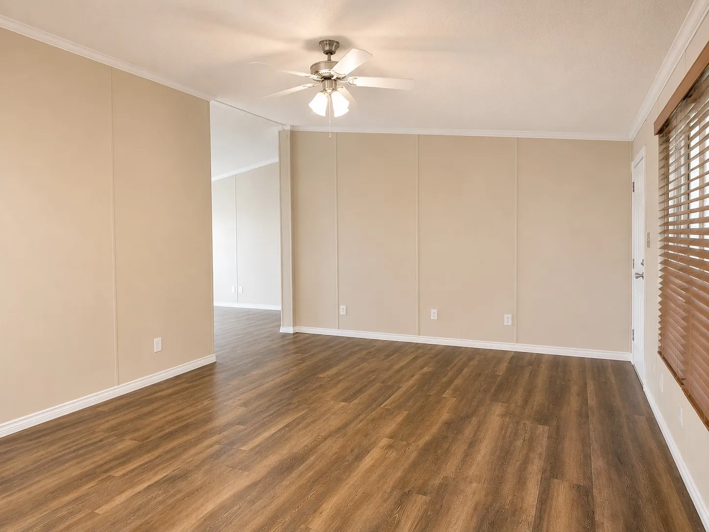 Spacious room featuring wood-finish flooring, light beige panel walls, white baseboards, and a ceiling fan with integrated lighting