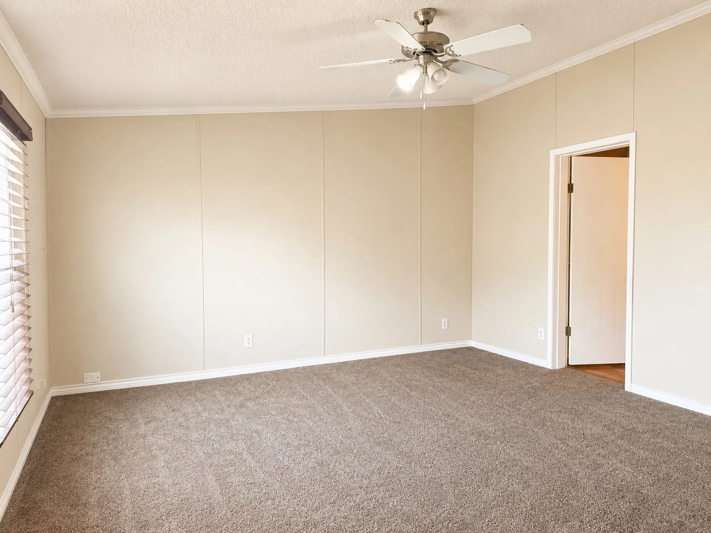 Spacious room featuring new carpeting, neutral wall paneling, white crown molding, and a ceiling fan with integrated lighting