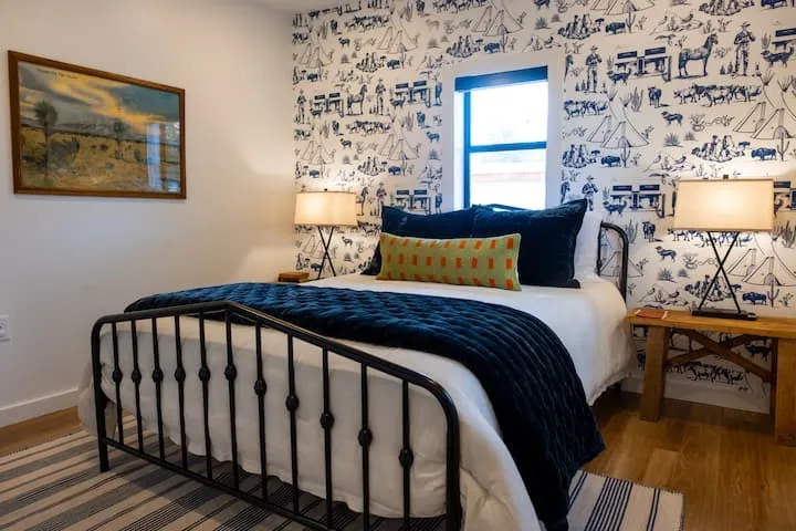 Bedroom featuring patterned wallpaper, light wood-finish flooring, and a black wrought iron bed frame