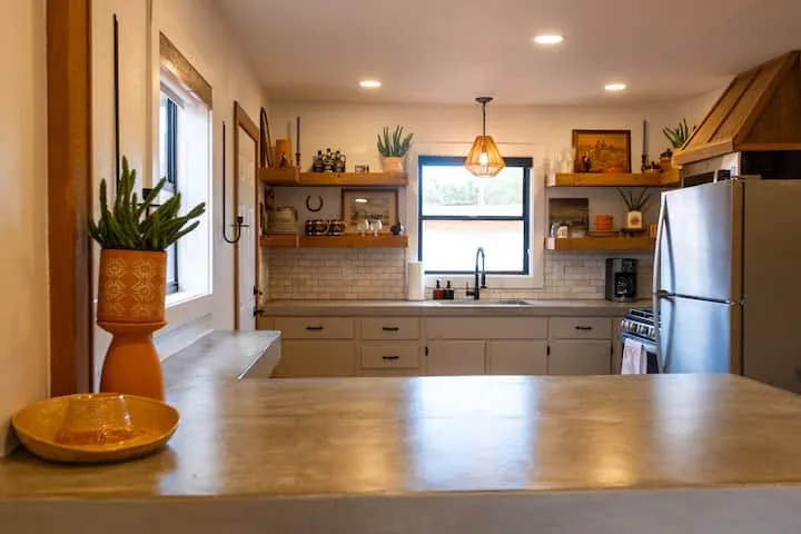 Kitchen featuring a large concrete countertop island, subway tile backsplash, open wood shelving, recessed lighting, and a wood-finish range hood