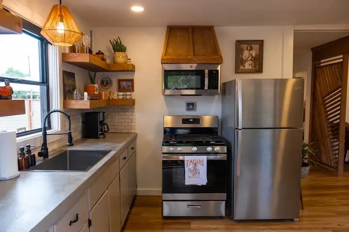 Modern kitchen featuring stainless steel appliances, concrete-finish countertops, and wood-finish open shelving