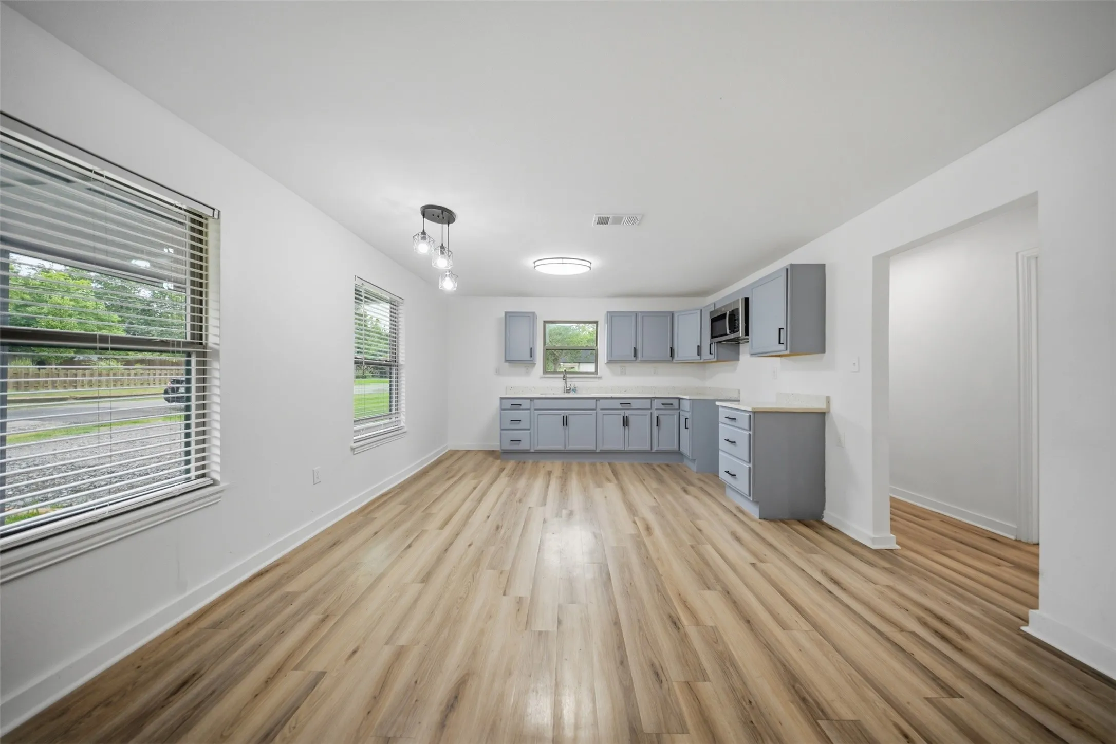 Open-concept kitchen and living area featuring wood-finish flooring, light gray cabinetry, and light countertops