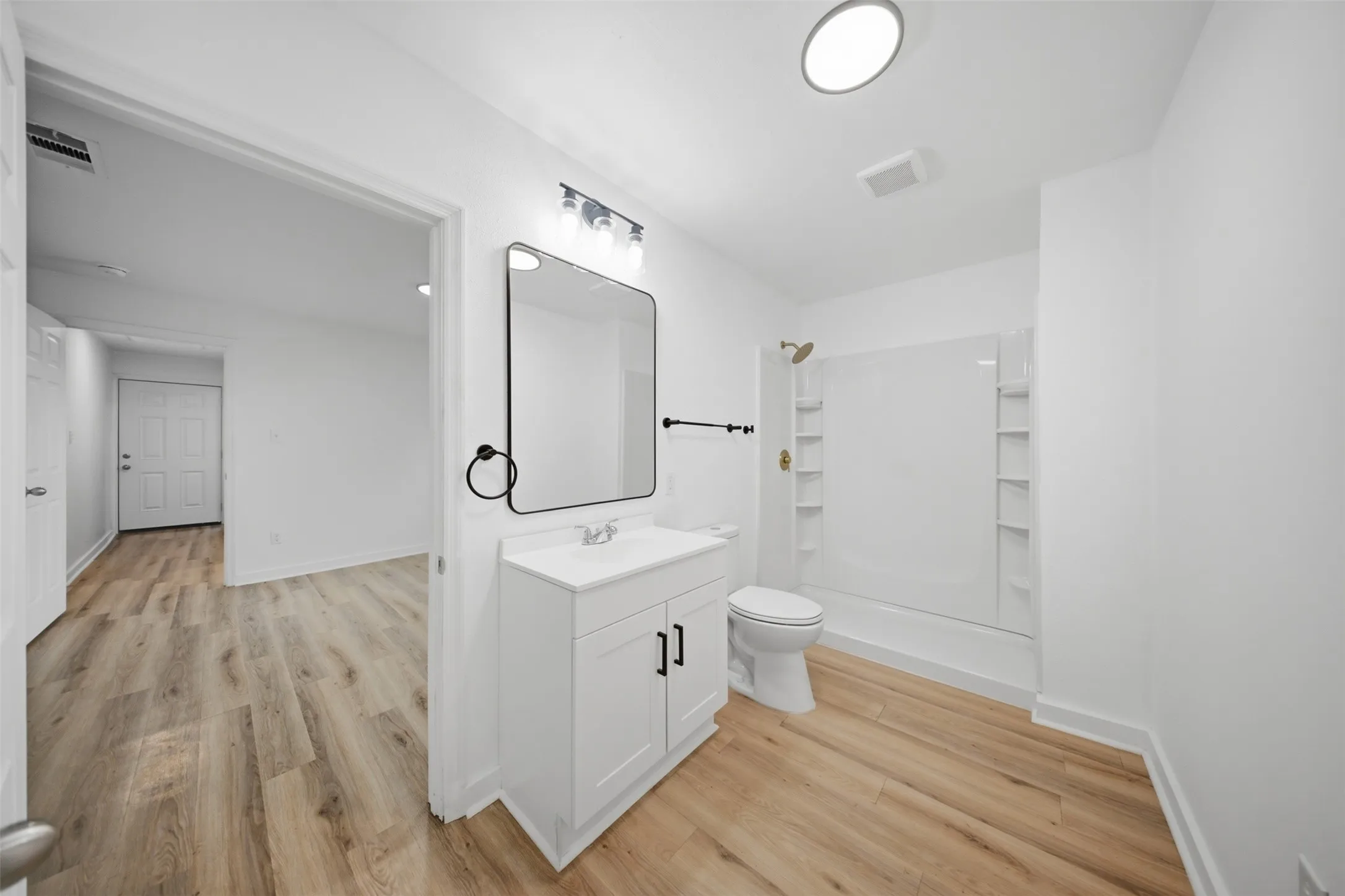 Bathroom featuring a white vanity with black hardware, a rectangular framed mirror, a tub/shower combination, and wood-finish flooring