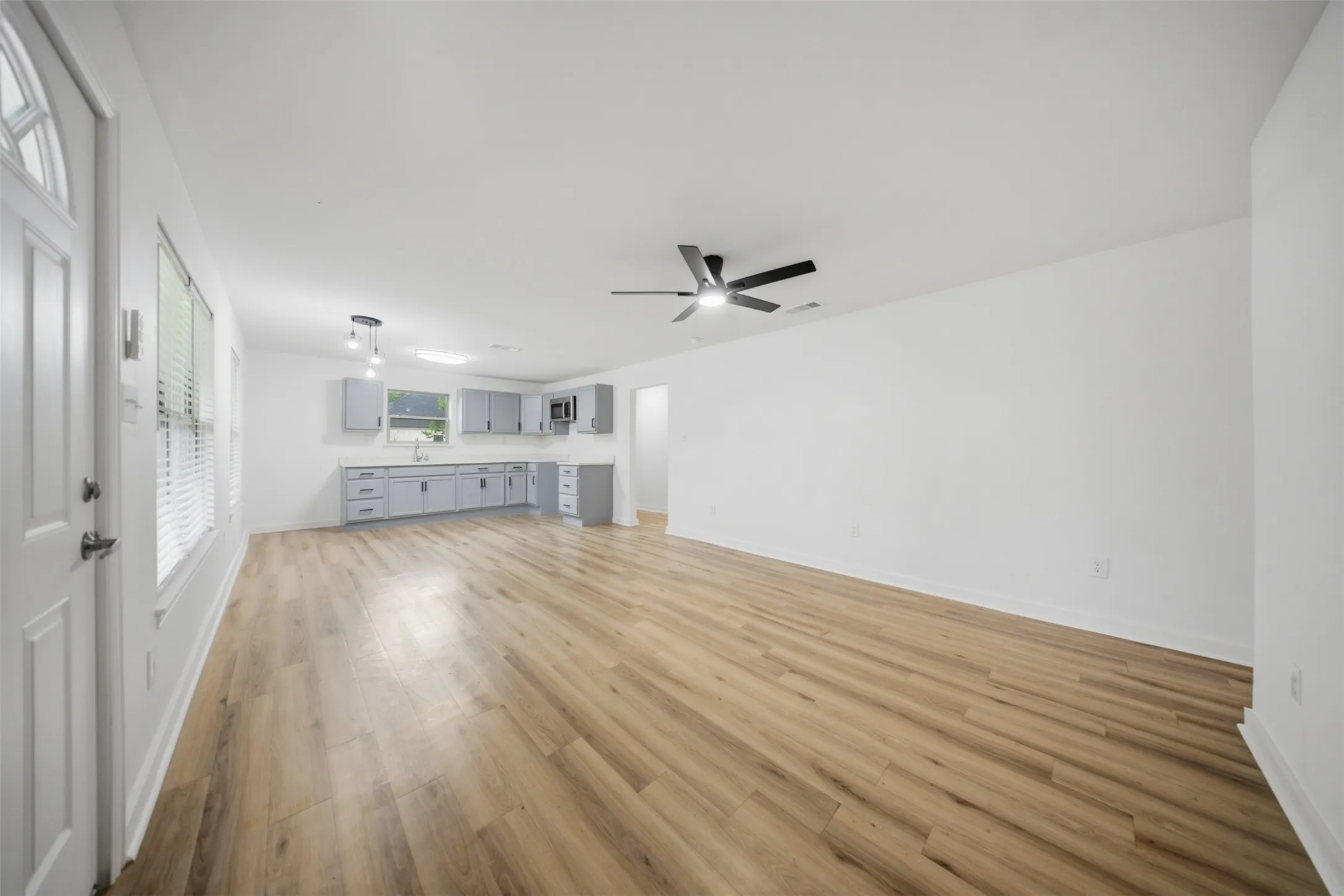 Open-concept living space featuring wood-finish flooring, white walls, and a ceiling fan