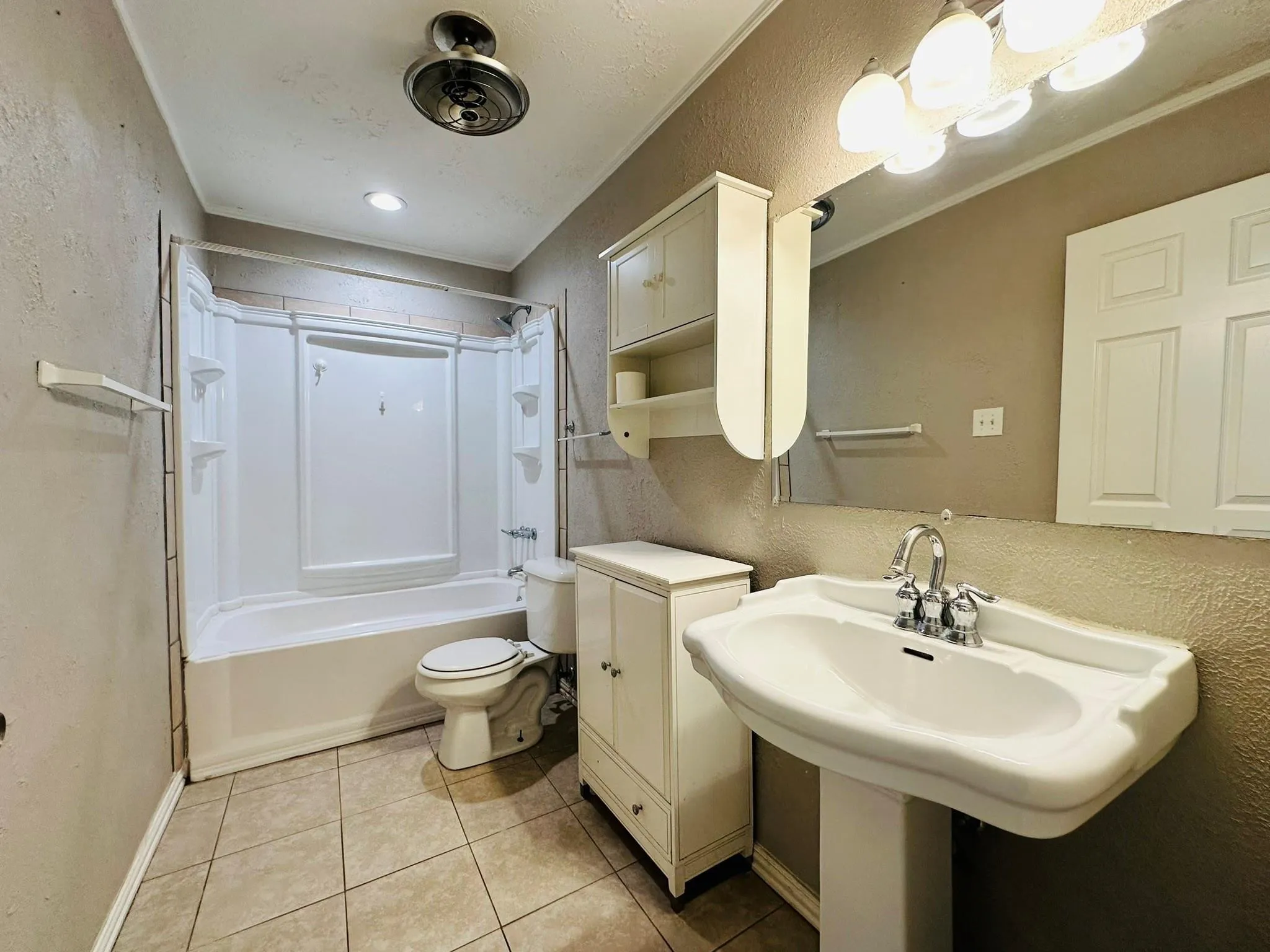 Bathroom featuring a pedestal sink, white tub-shower combination, tiled flooring, and wall-mounted cabinetry