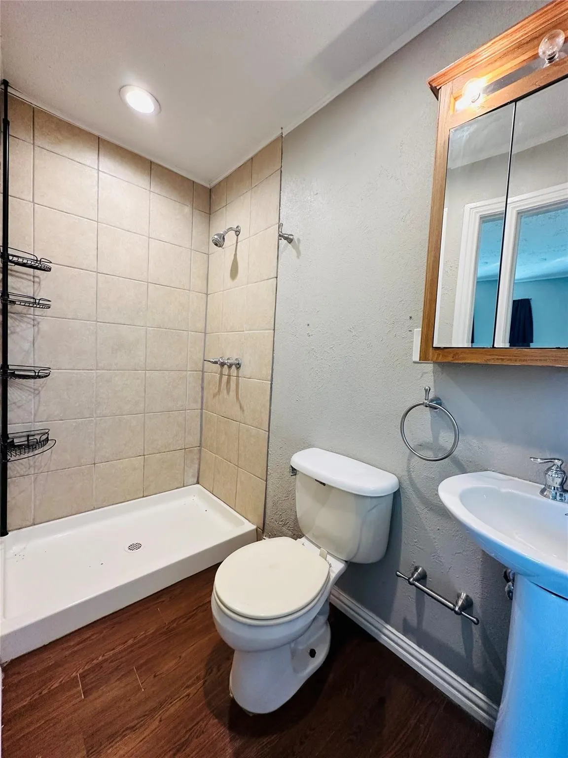 Bathroom featuring a stand-up shower with tiled surround, wood-finish flooring, a pedestal sink, and a mirrored medicine cabinet