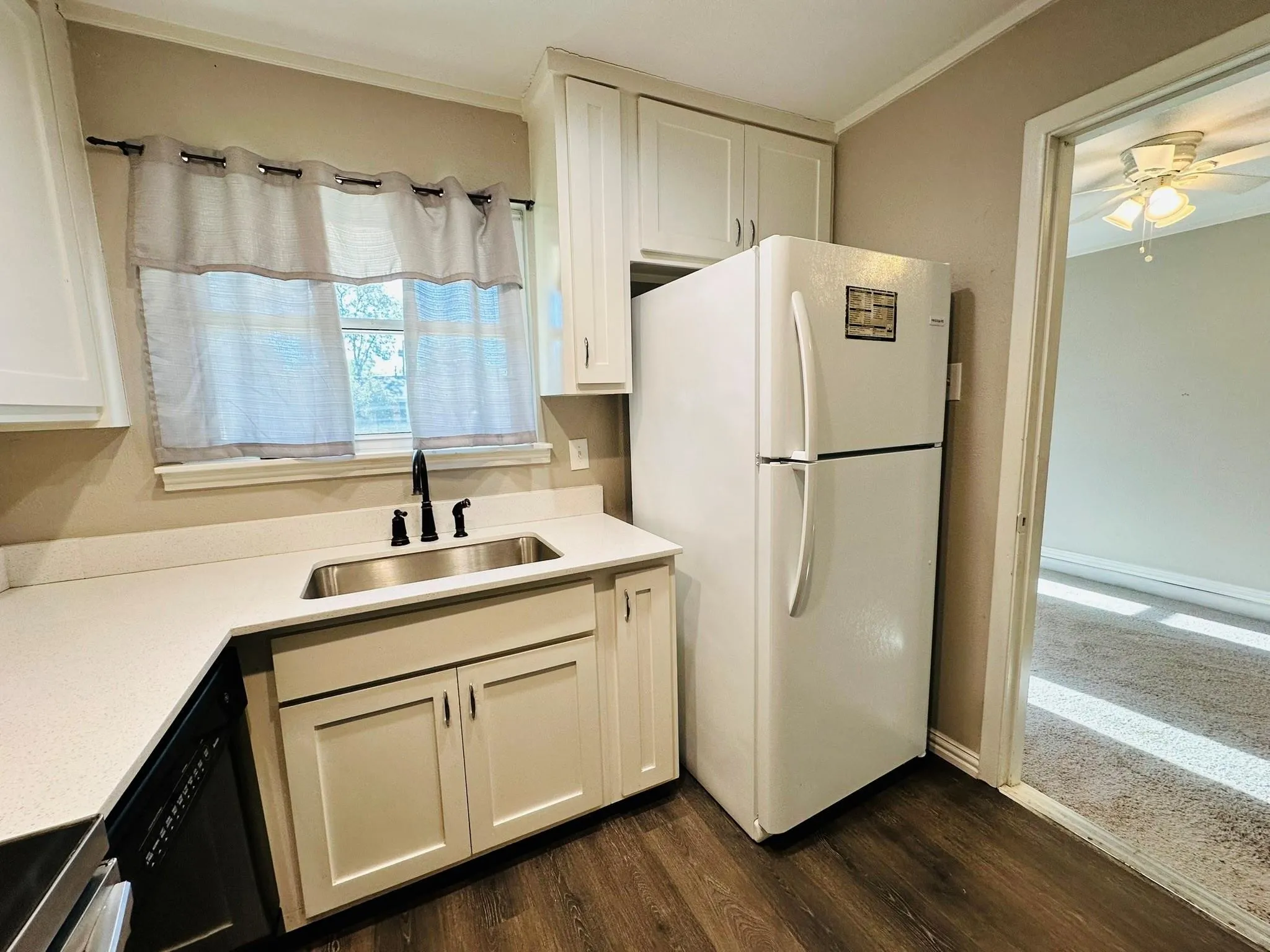Kitchen featuring L-shaped white countertops, a stainless steel sink with a matte black faucet, white cabinetry, and wood-finish flooring