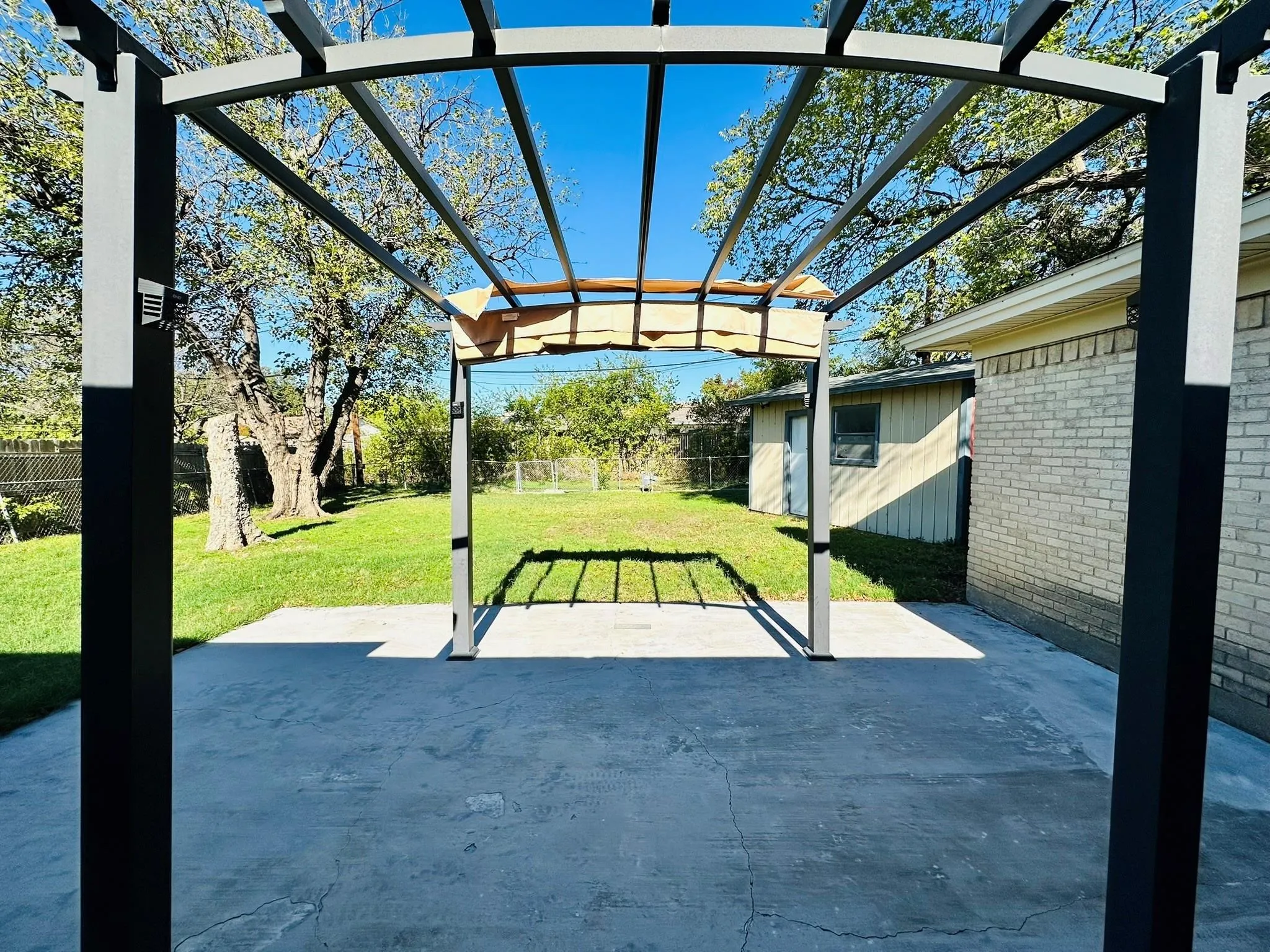 Backyard patio with a dark-framed pergola over a concrete slab