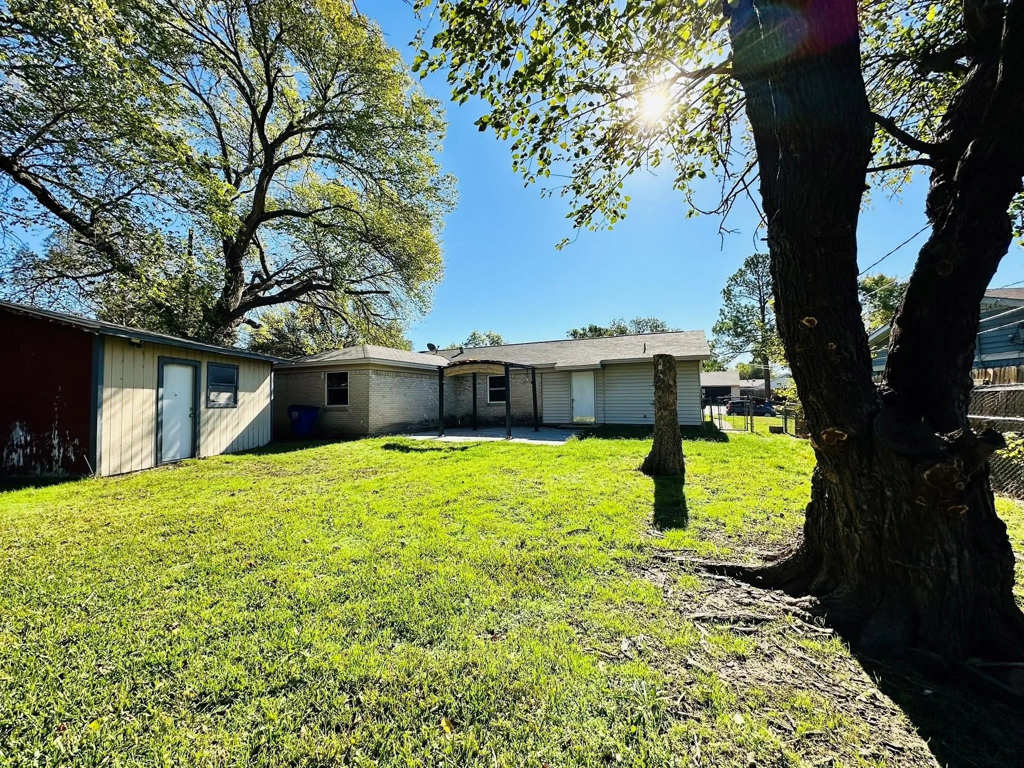 Spacious backyard with a covered patio, a detached storage shed, and mature trees