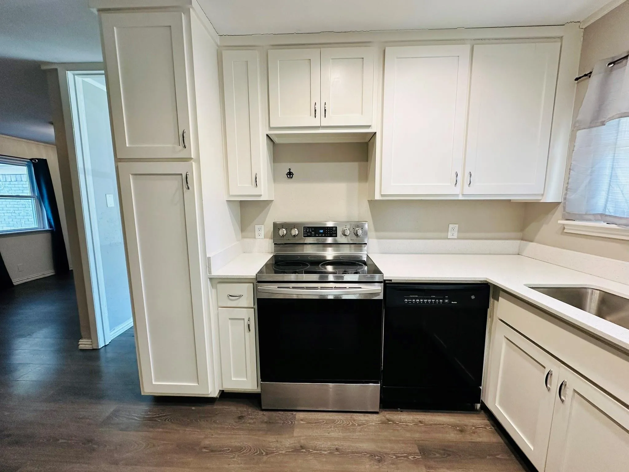 Kitchen featuring white shaker-style cabinetry, light-colored countertops, stainless steel appliances, and wood-finish flooring