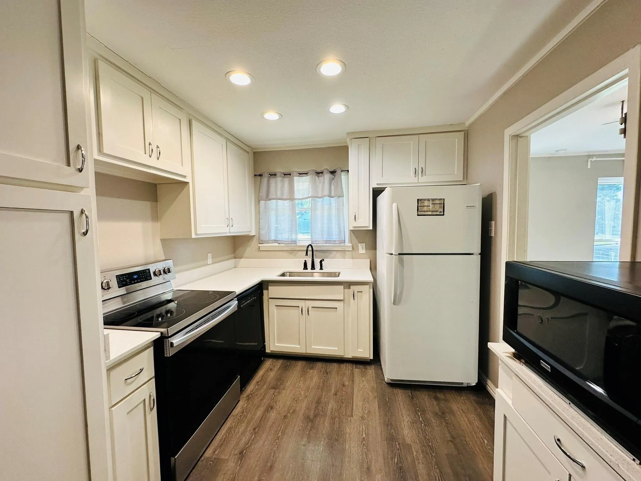 Contemporary kitchen featuring white cabinetry, light-toned countertops, a stainless steel electric range, a stainless steel faucet, and wood-finish flooring