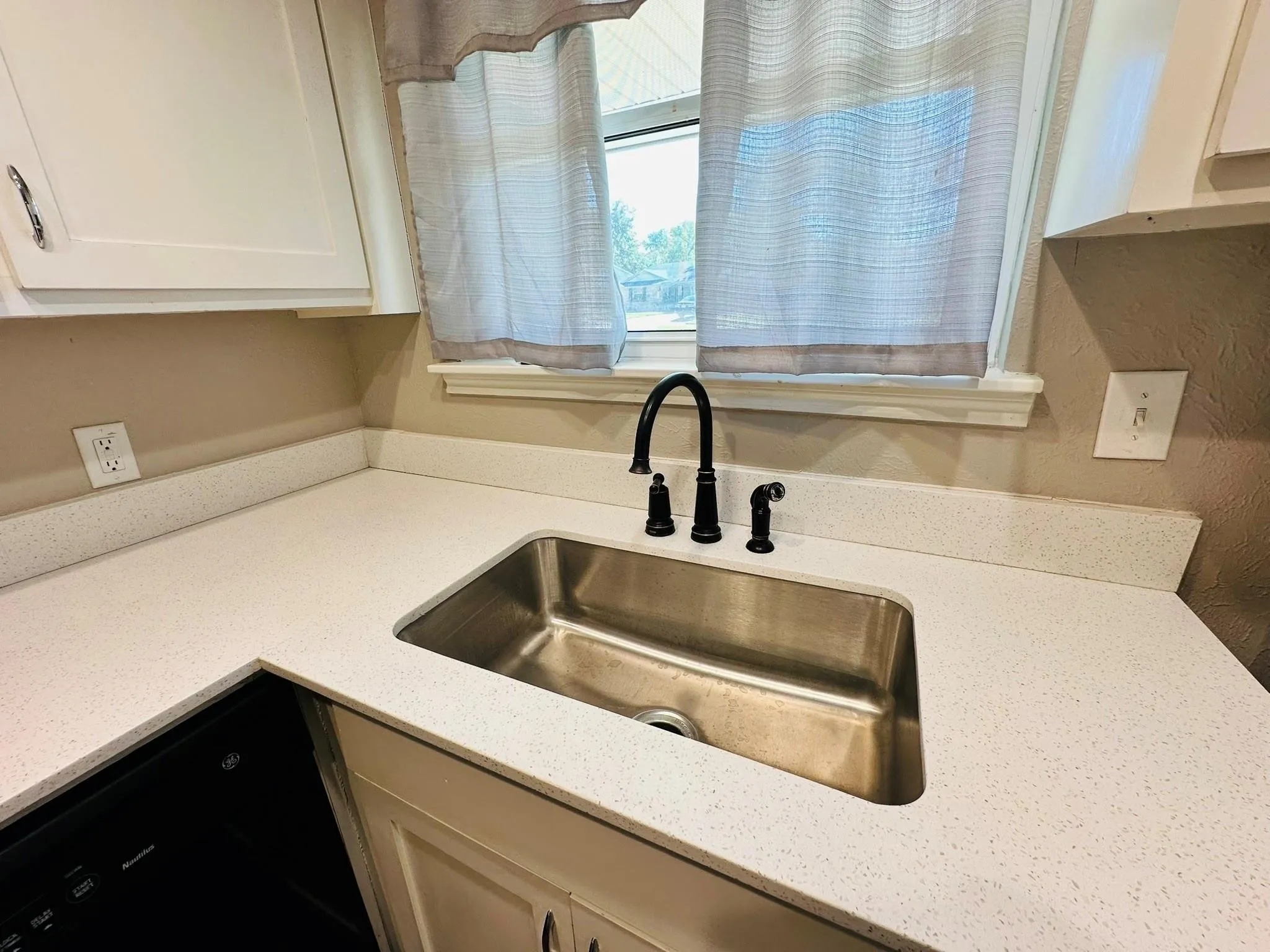 Kitchen featuring light-toned countertops, a stainless steel undermount sink, and a matte black gooseneck faucet