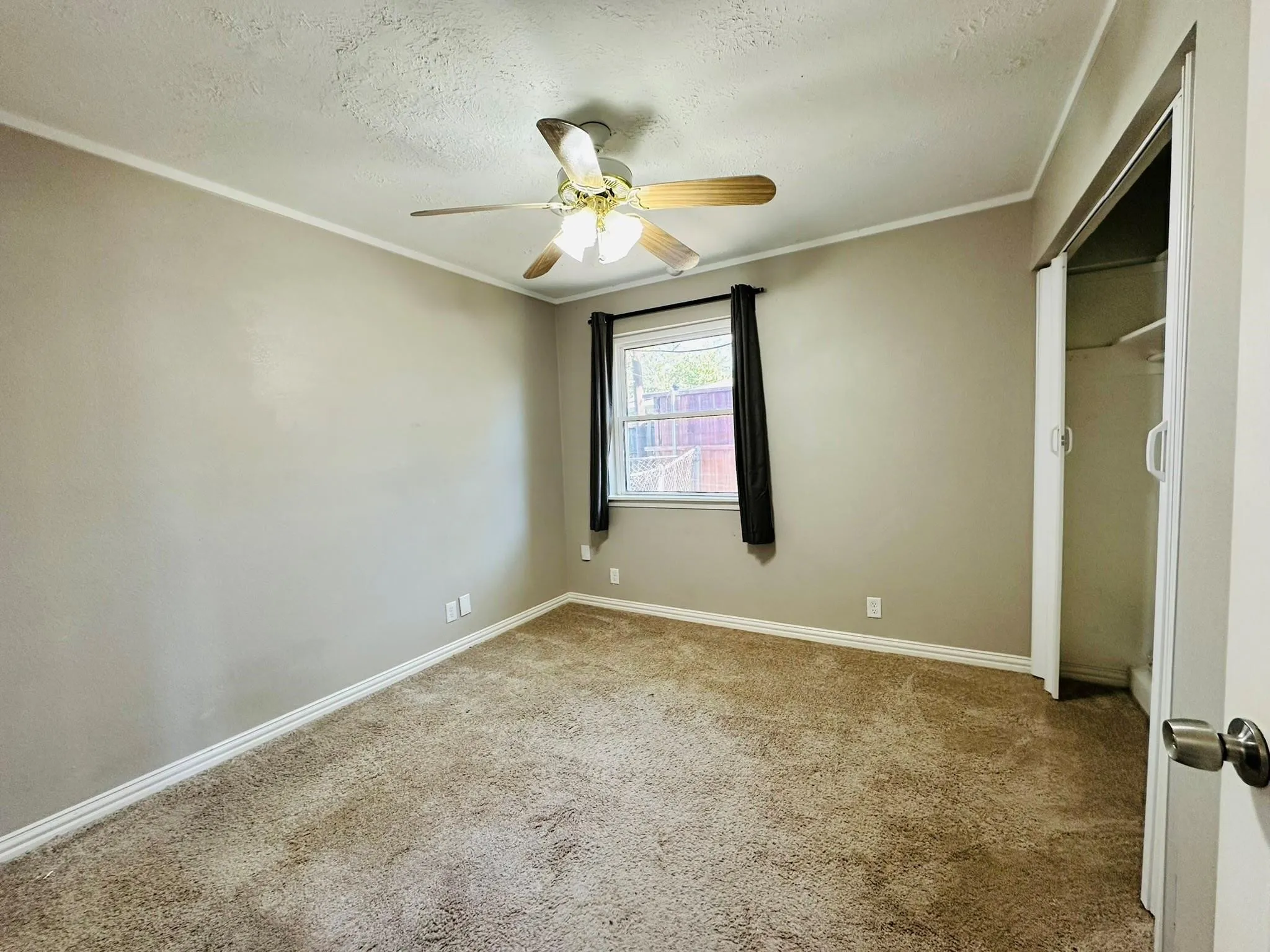 Carpeted room featuring a ceiling fan with integrated lighting, a window with dark drapes, and a closet with bifold doors