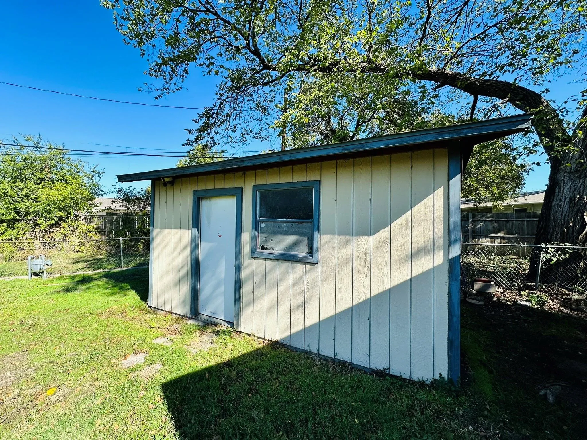 Detached shed structure with vertical siding, a single window, and a white entry door
