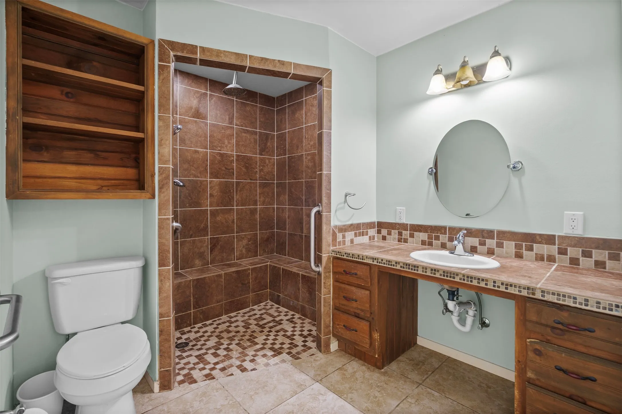 Spacious bathroom featuring a multi-head shower with a built-in bench, tiled walls, and a mosaic-patterned floor