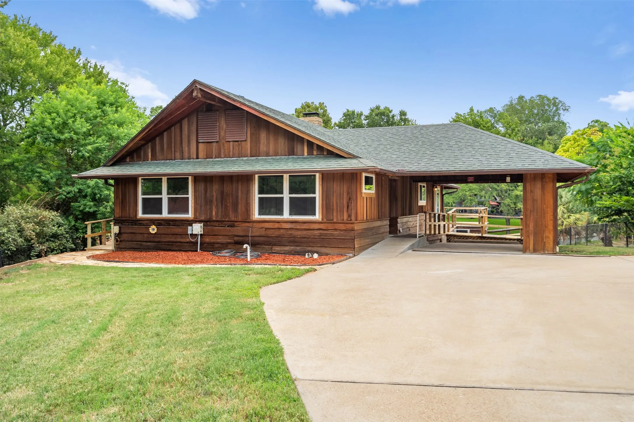 Wood-paneled home with a covered carport, ramp access, and a concrete driveway