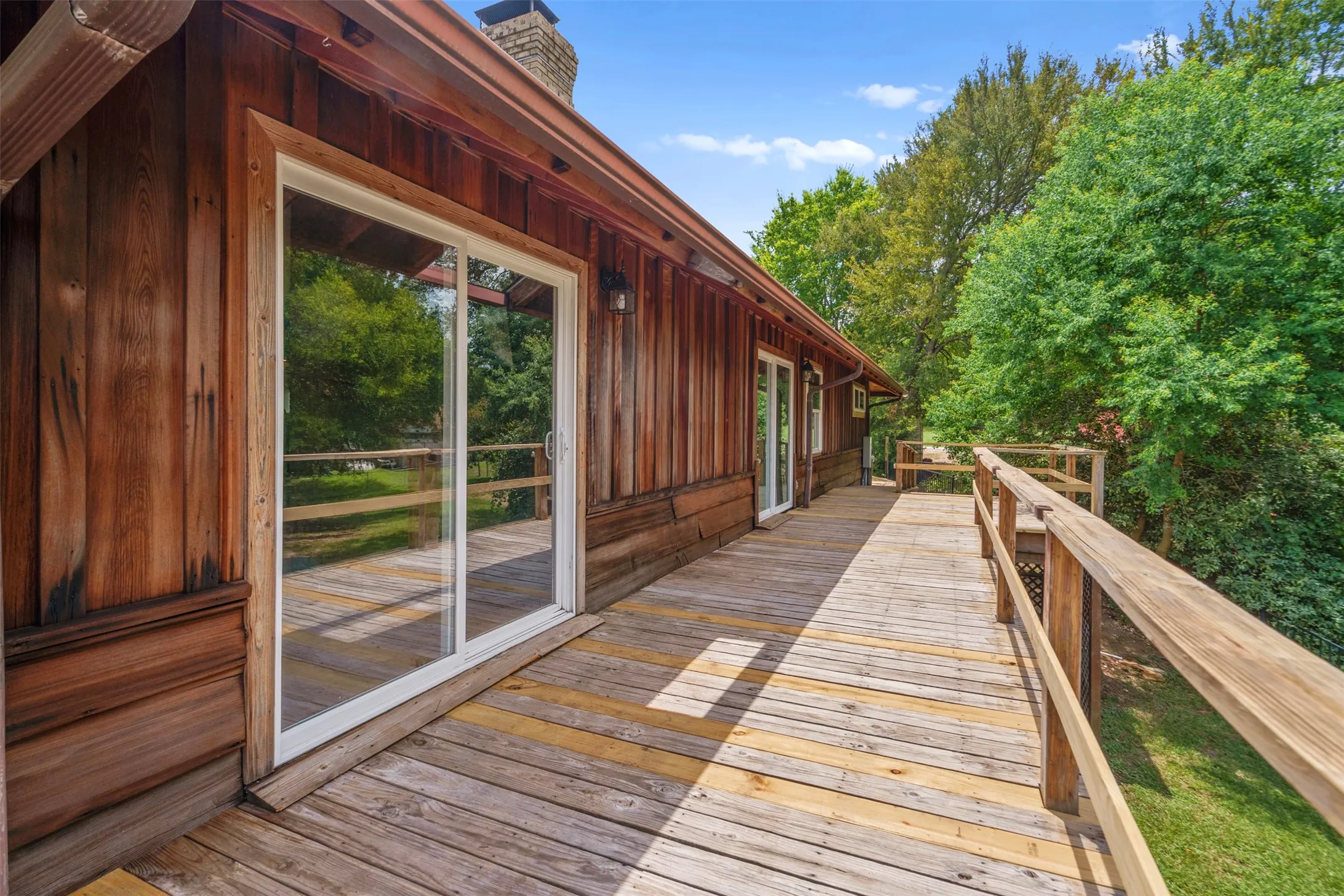 Expansive wood deck with a full-length railing, featuring multiple sliding glass doors and natural wood siding
