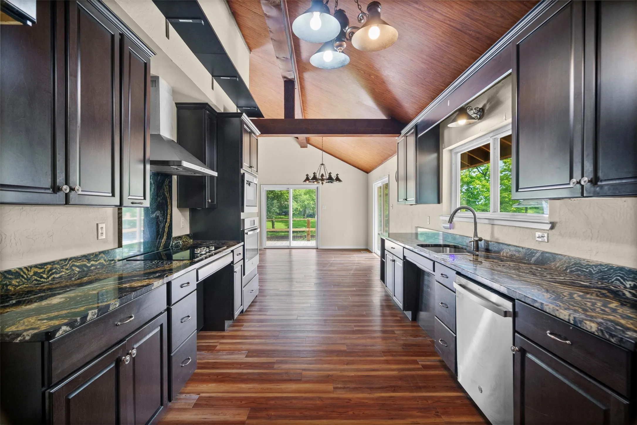 Spacious kitchen featuring dark cabinetry, patterned countertops, stainless steel appliances, and wood-finish flooring
