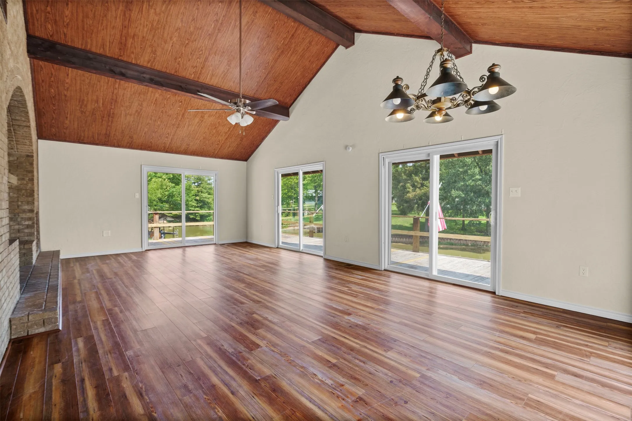 Spacious room featuring a vaulted wood-paneled ceiling with exposed beams, wood-finish flooring, and multiple sliding glass doors