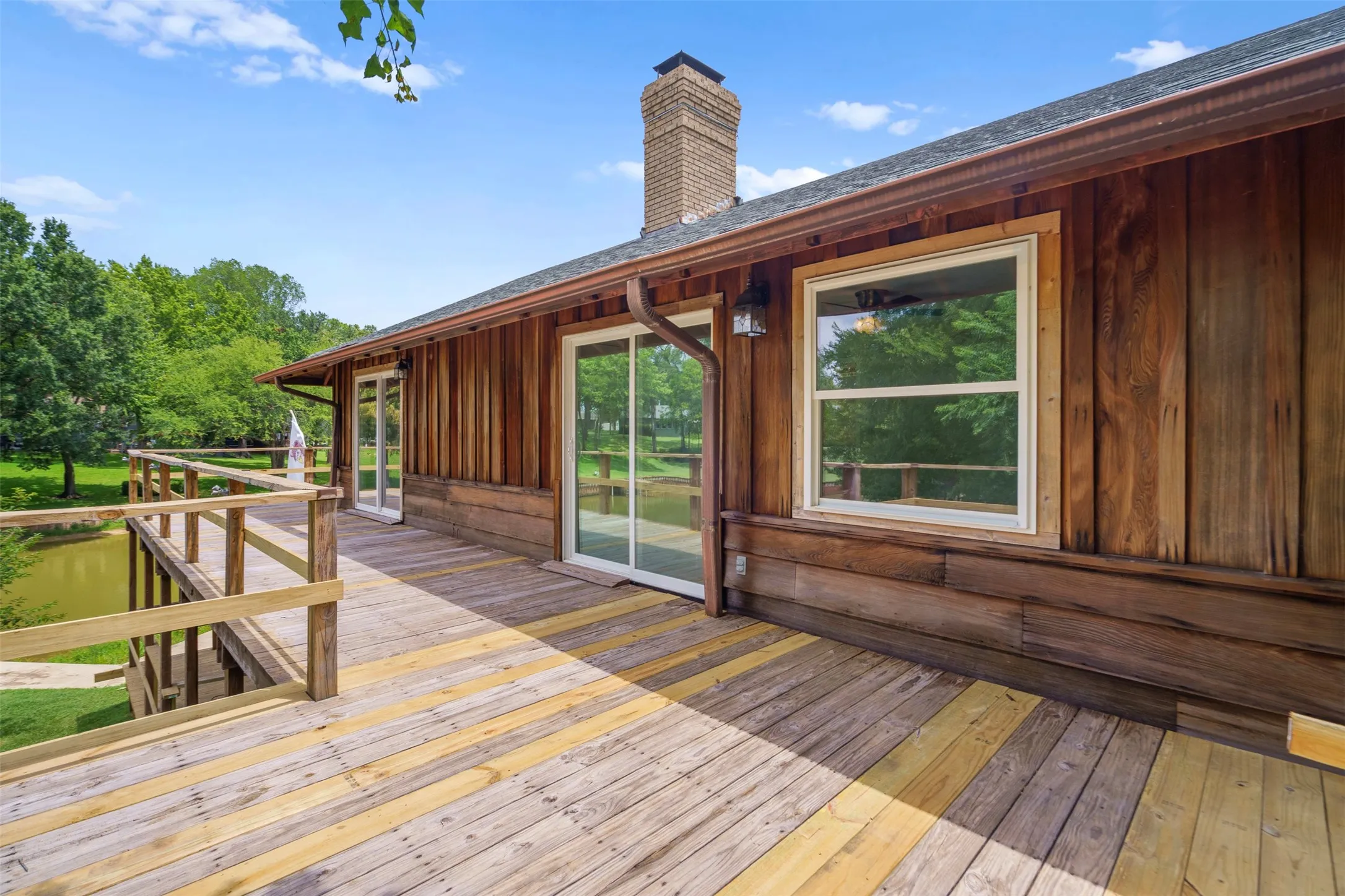Spacious outdoor deck featuring wood flooring and railings, offering expansive views of the surrounding trees and pond