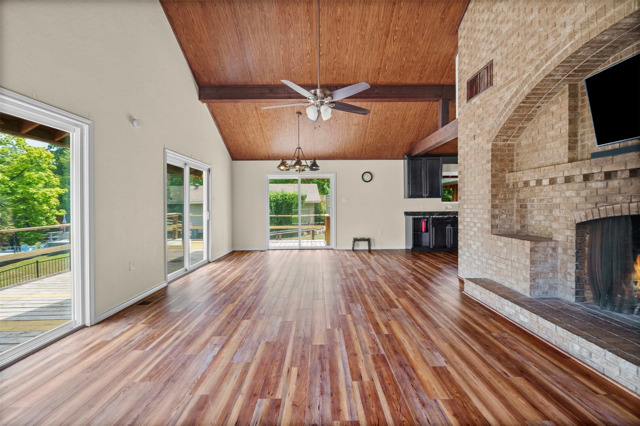 Spacious interior featuring wood-finish flooring, a vaulted wood-paneled ceiling with exposed beams, and multiple sliding glass doors