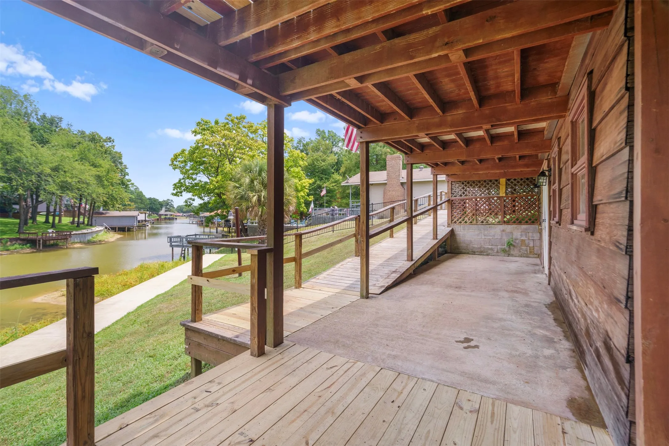 Covered porch with exposed wood beams, featuring a concrete pad and wood decking