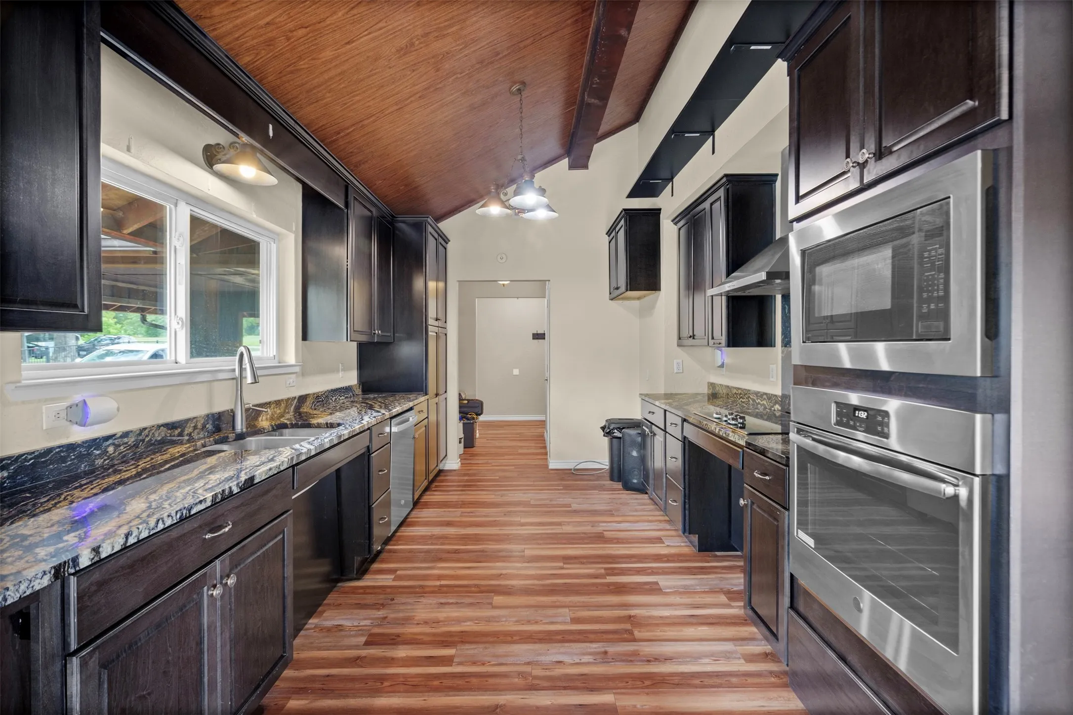 Kitchen featuring wood-finish flooring, dark cabinetry, granite countertops, and stainless steel built-in appliances