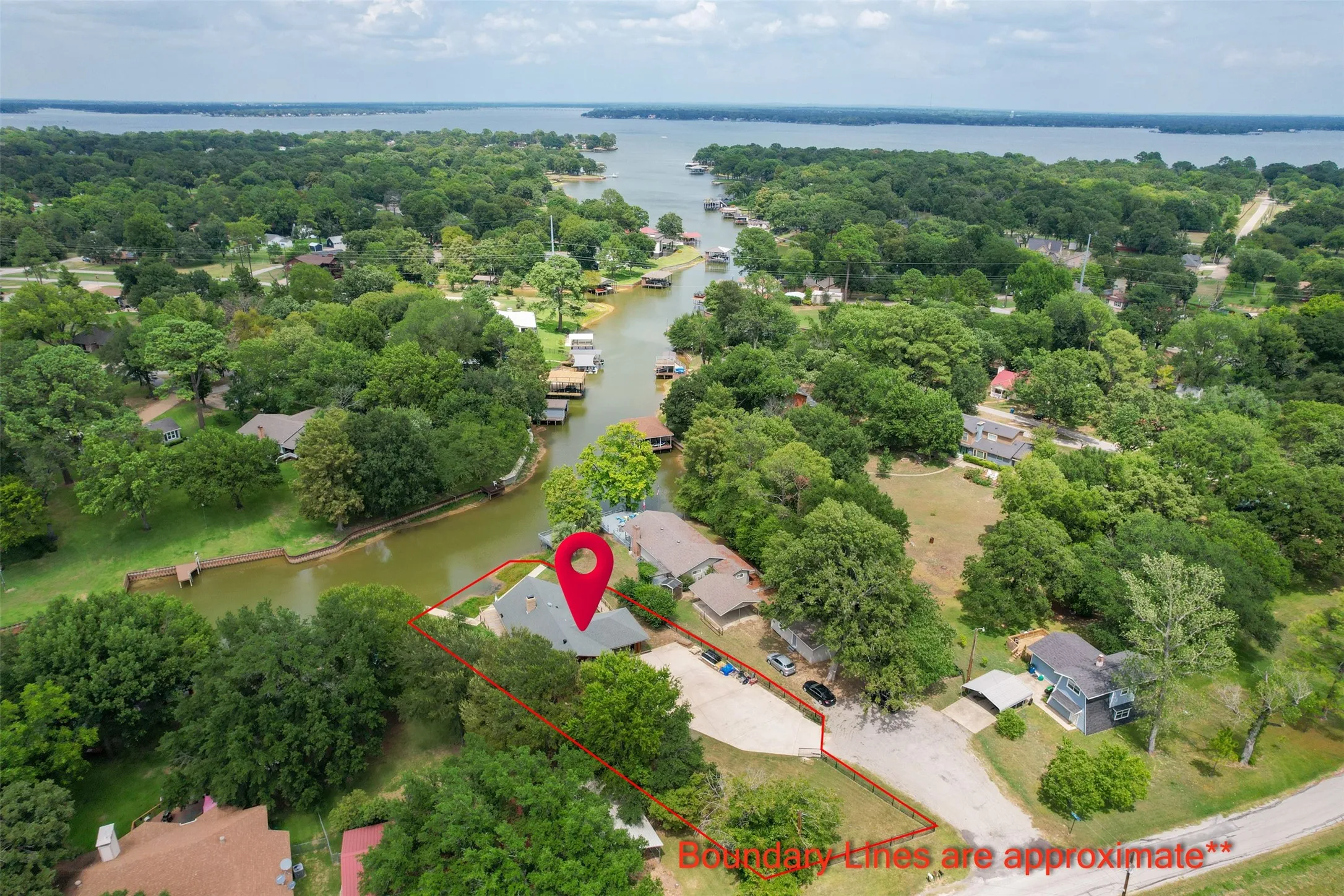 Waterfront property featuring a canal leading to a large lake, mature trees, a private boat dock, and a dedicated parking area