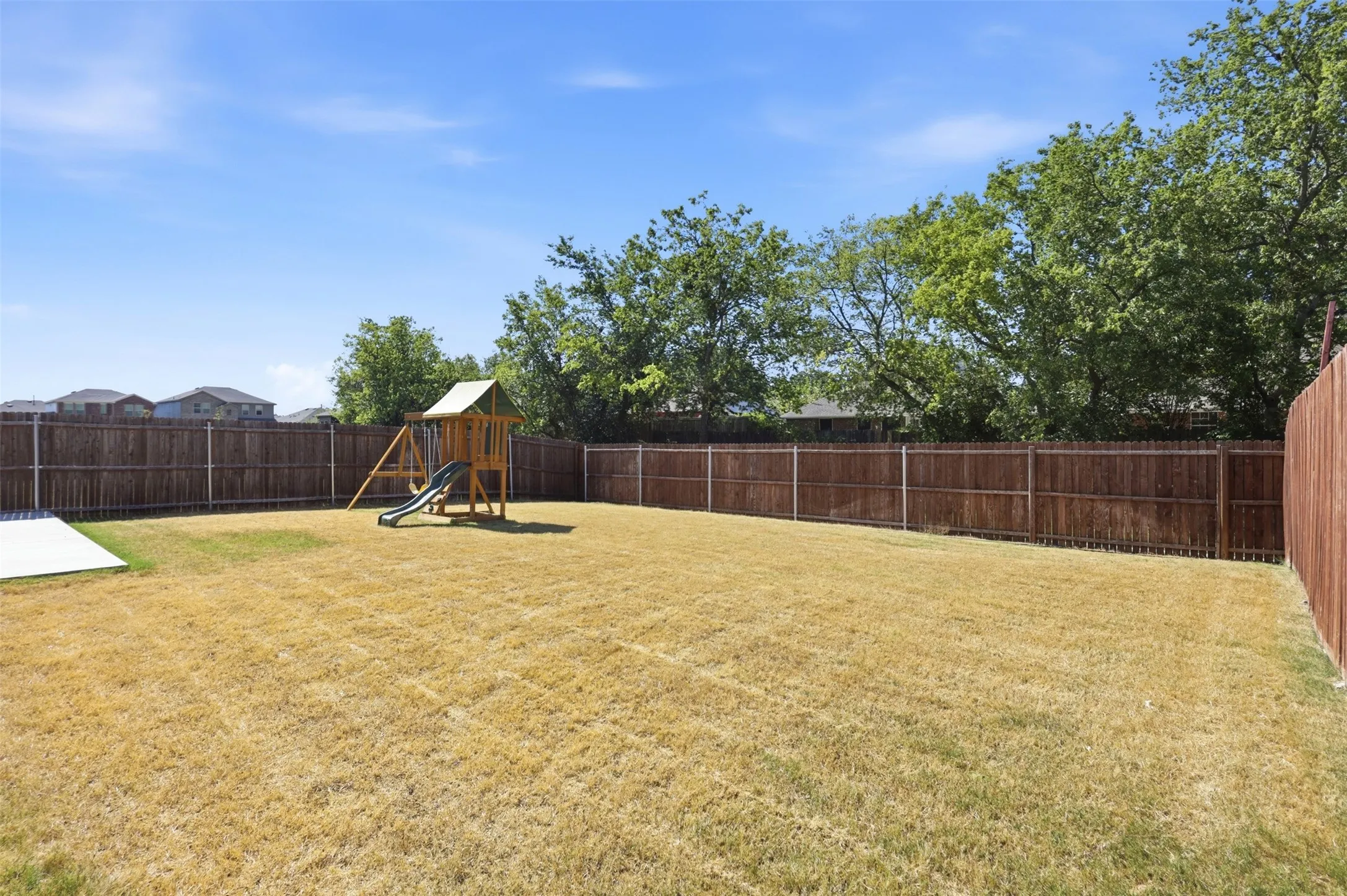 Expansive backyard featuring a full privacy fence, mature trees beyond the fence line