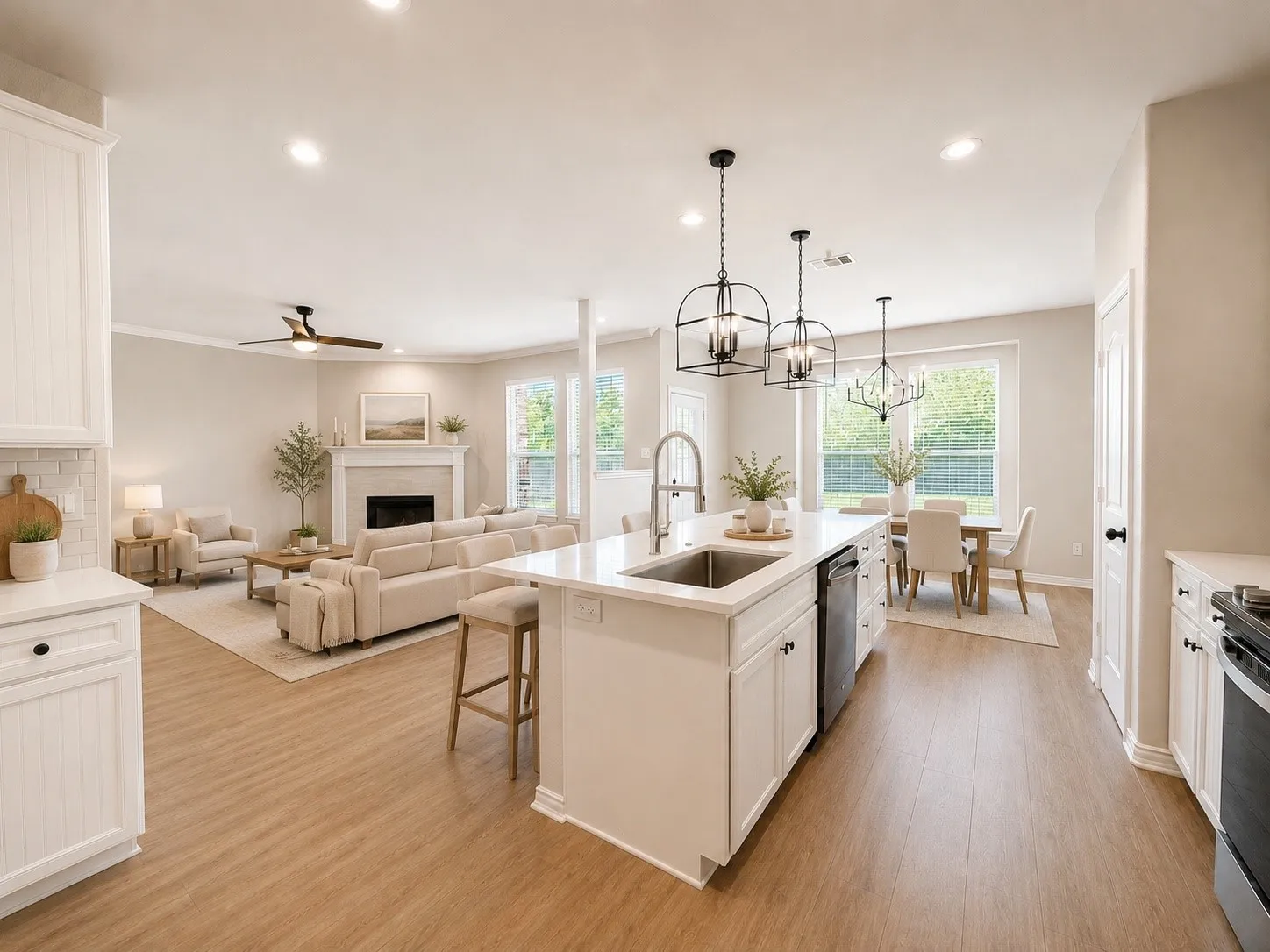 Open-concept living space featuring wood-finish flooring, a white kitchen island with an undermount sink, recessed lighting, and a fireplace with a mantel