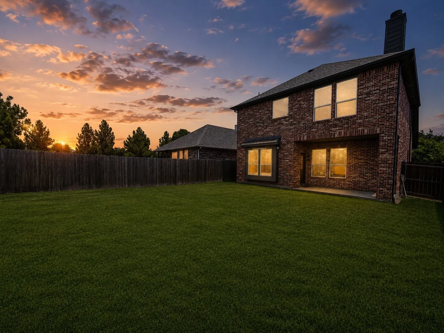 Expansive backyard featuring a manicured lawn, full privacy fencing, and mature perimeter trees