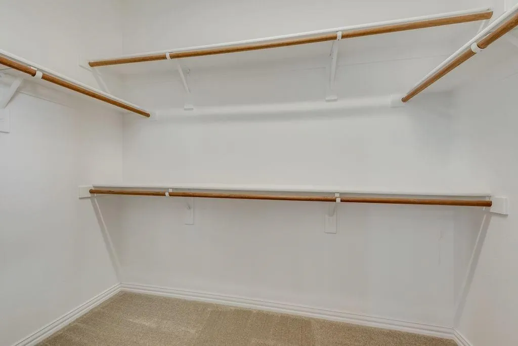 Walk-in closet featuring light-colored carpeting, white baseboards, and built-in white shelving with wooden hanging rods