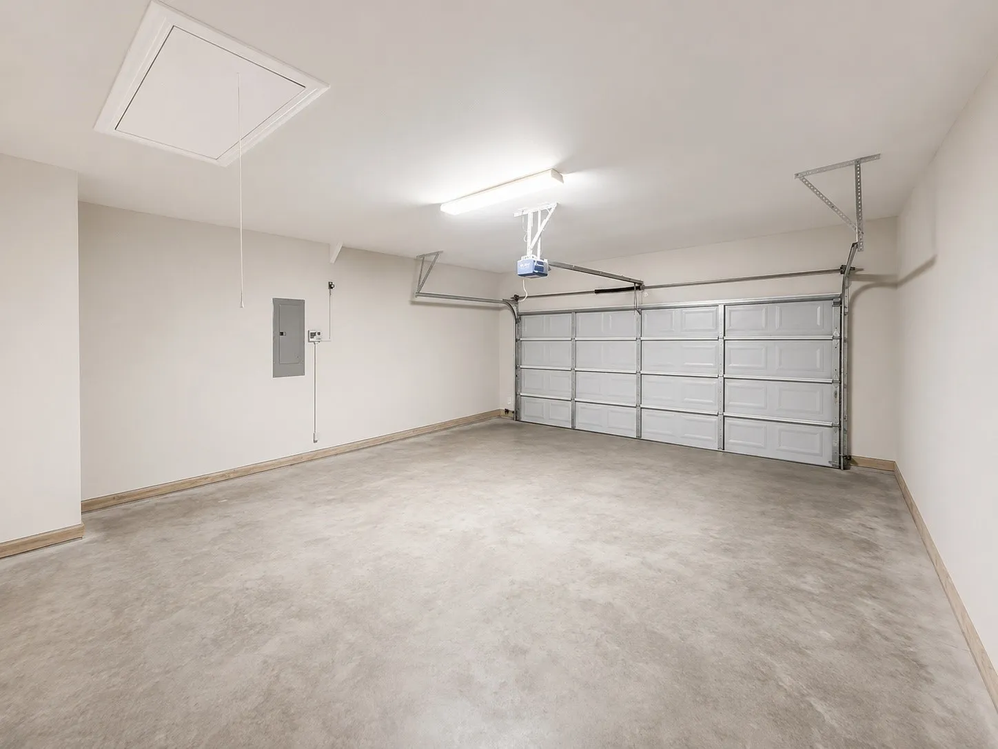 Spacious two-car garage featuring a concrete floor, automatic garage door opener, and overhead fluorescent lighting