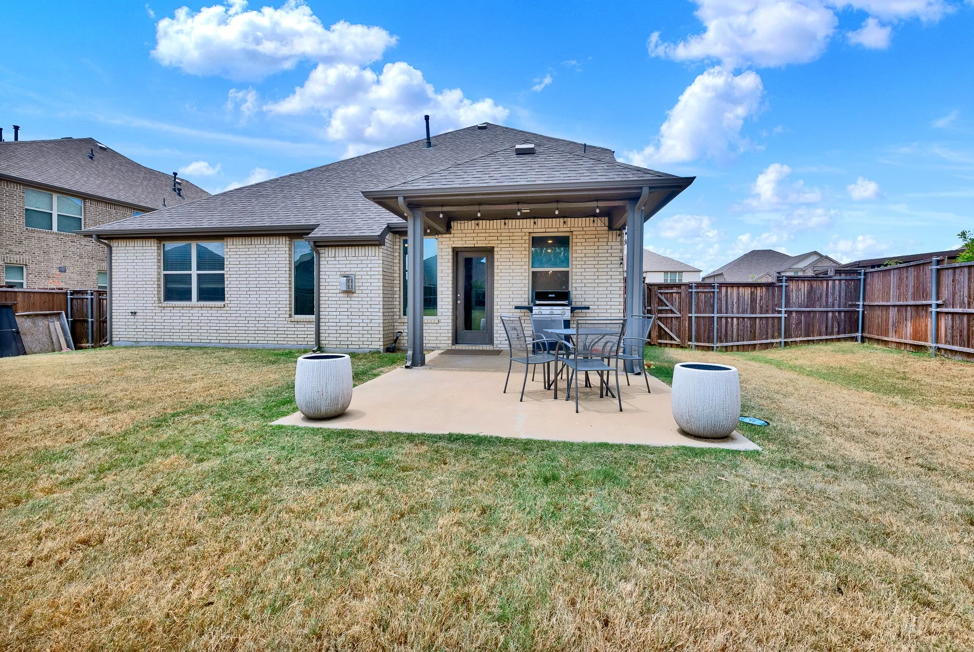 Spacious backyard featuring a covered patio, paved concrete surface, and light brick exterior