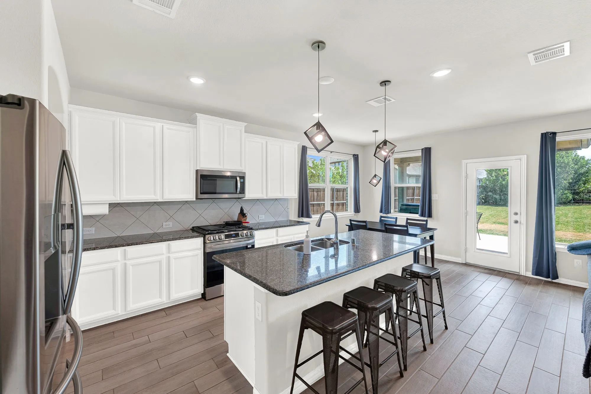 Modern kitchen featuring an island with a double basin sink, stainless steel appliances, white cabinetry, and wood-finish flooring