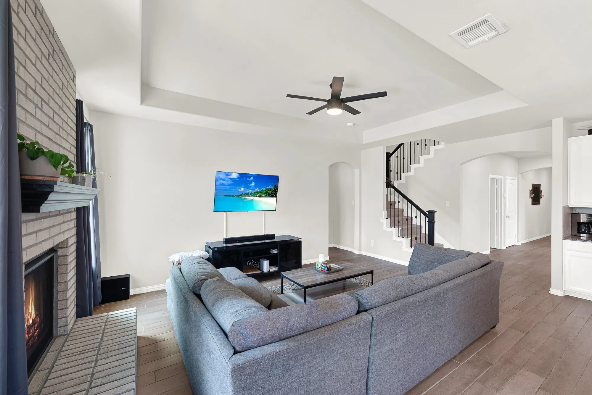 Living area featuring light wood-finish flooring, a brick fireplace with a dark mantel, and a ceiling fan