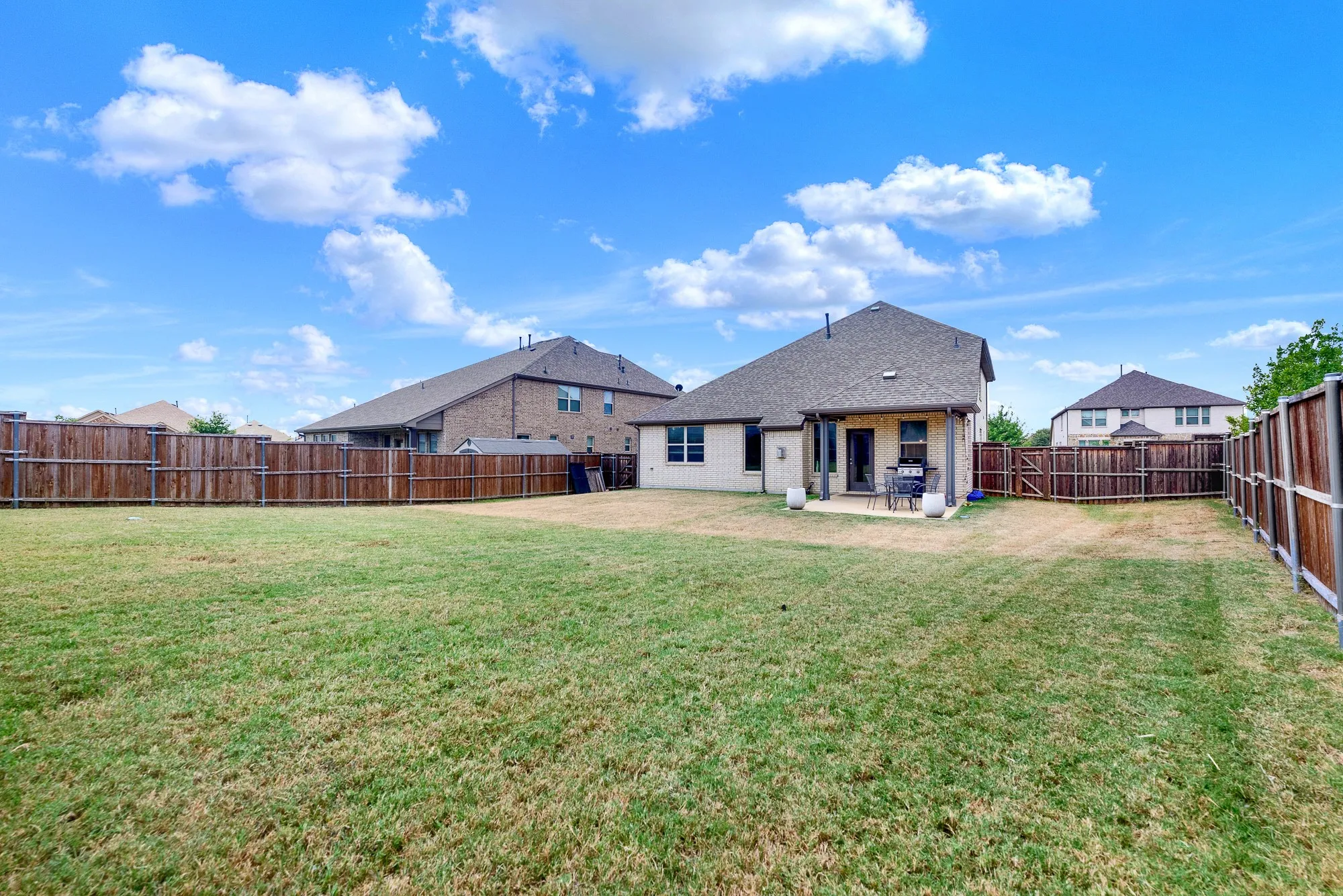 Expansive backyard featuring a large grass area, wood privacy fencing, and a covered patio