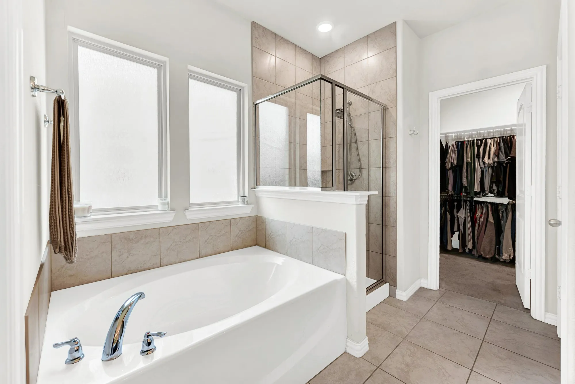 Bathroom featuring a built-in tub with chrome fixtures, a tiled shower with a glass enclosure, and two privacy windows
