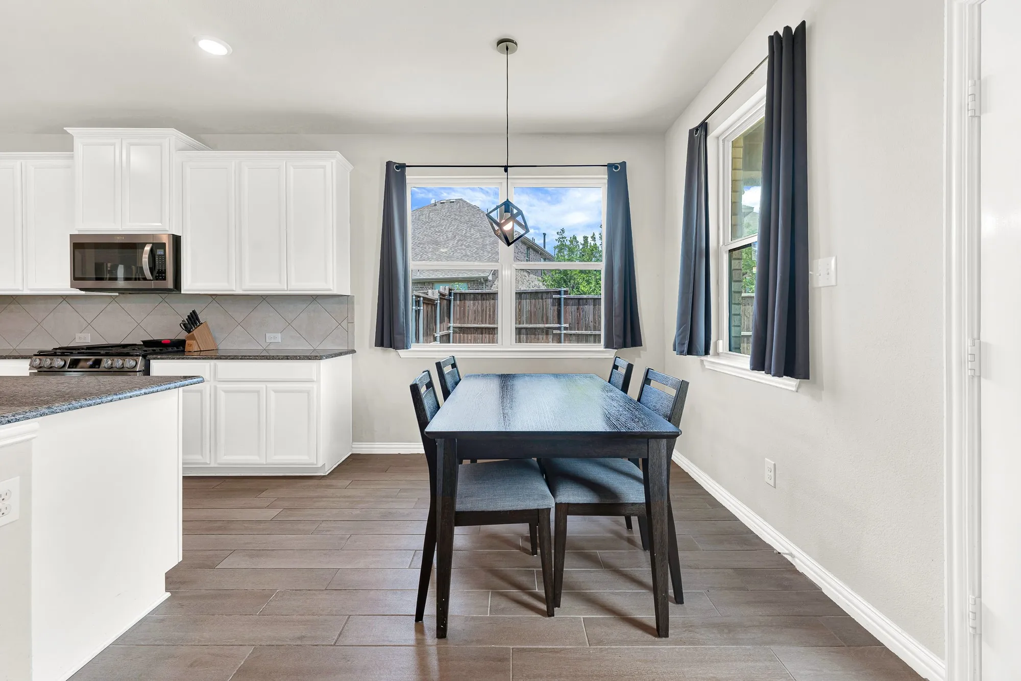 Open-concept dining area featuring wood-finish flooring, two large windows, and a modern geometric pendant light fixture