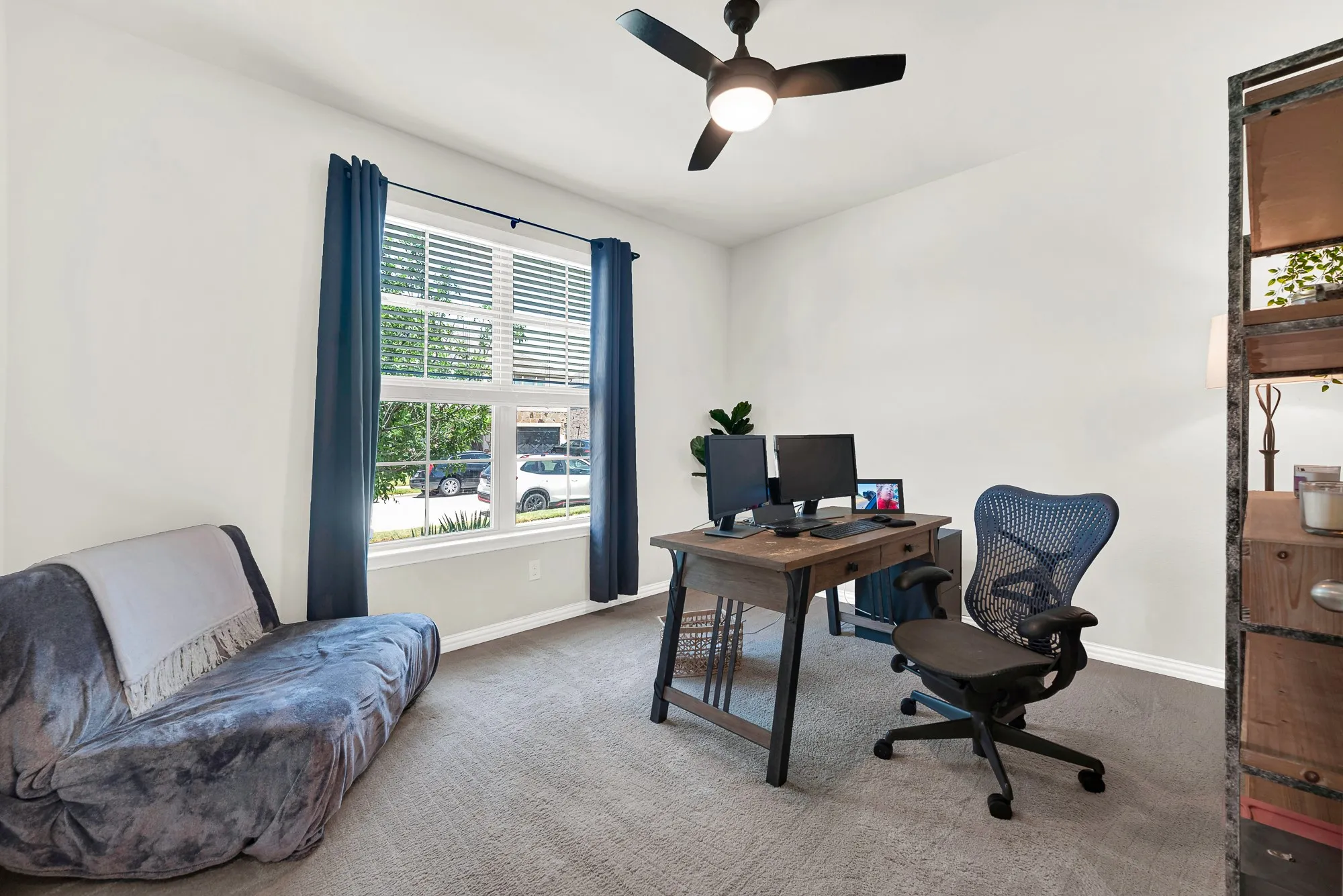 Carpeted room featuring a ceiling fan with integrated lighting, a large window with blinds and dark curtains, and white wall finishes