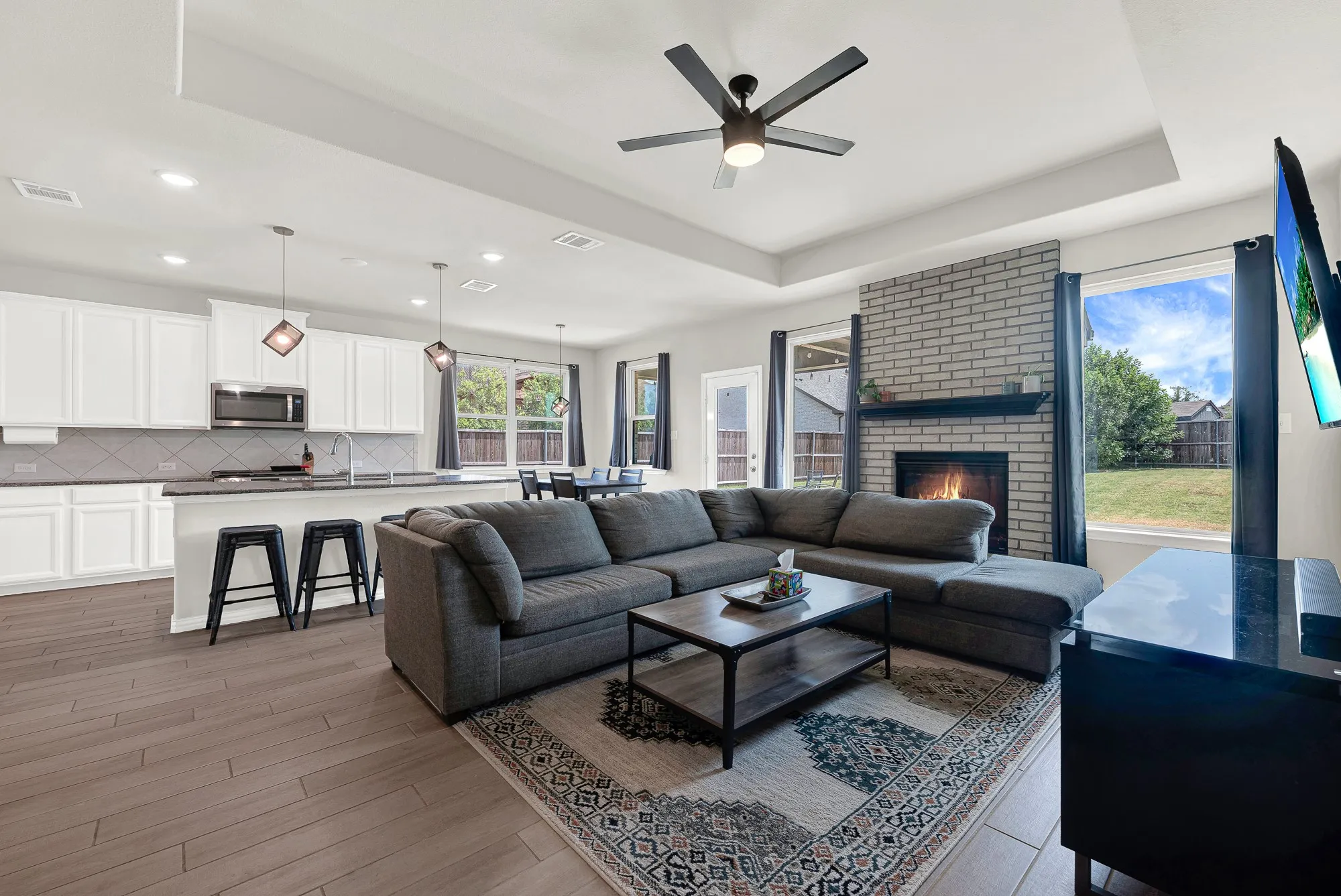 Open-concept living area with wood-finish flooring, a tray ceiling, and recessed lighting